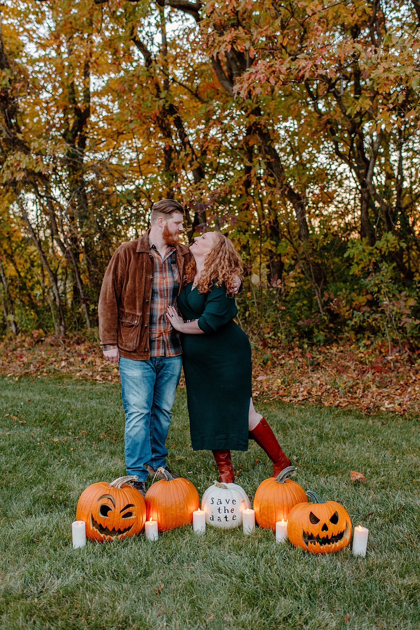  Man and woman kiss standing behind pumpkins at Halloween engagement session 
