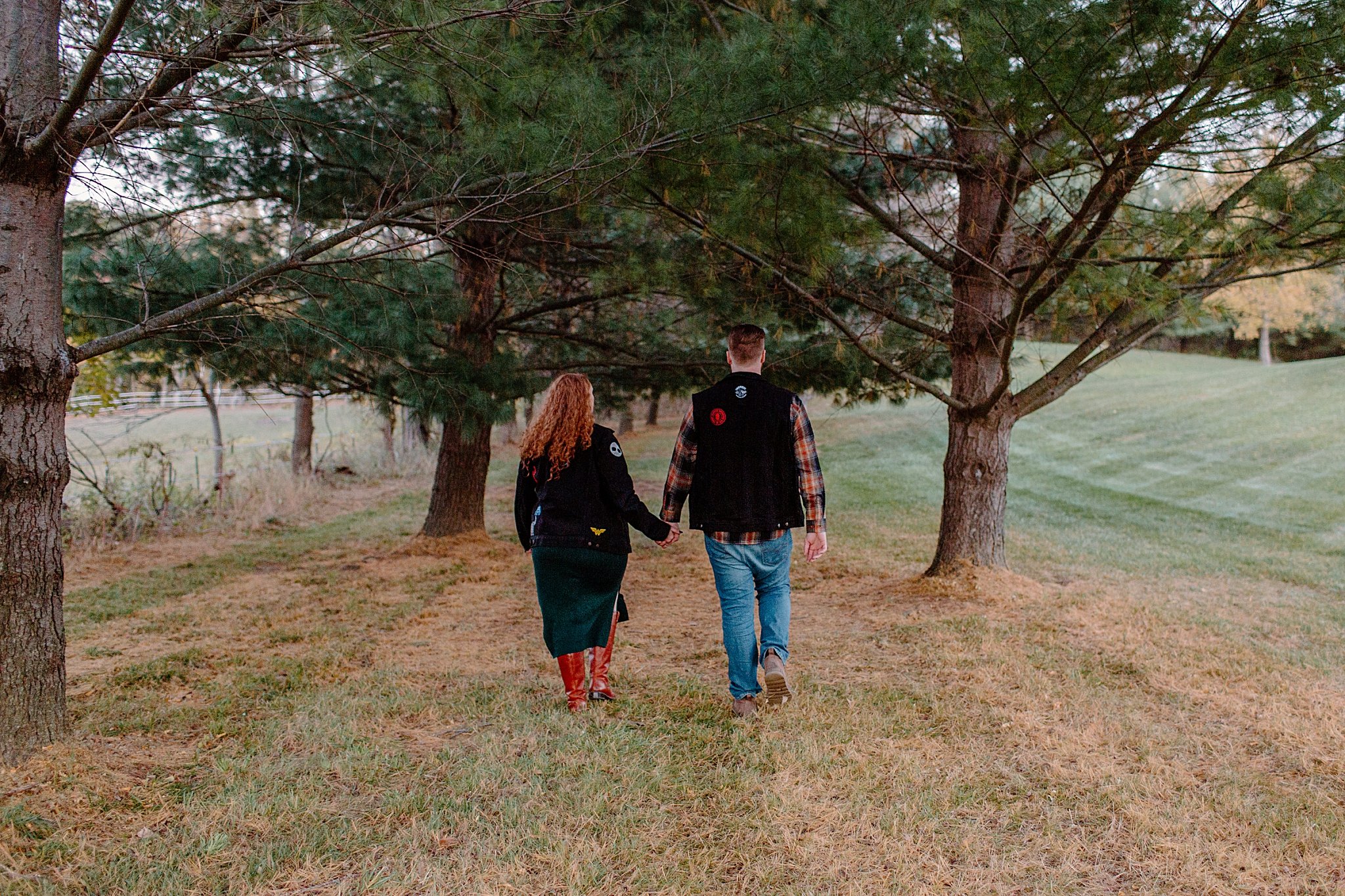  Man and woman walk between trees holding hands at Halloween engagement session 