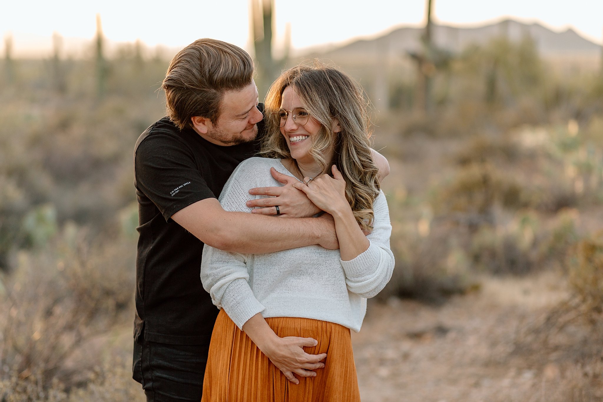 dad-to-be wraps arms around mom-to-be during Gates Pass session 