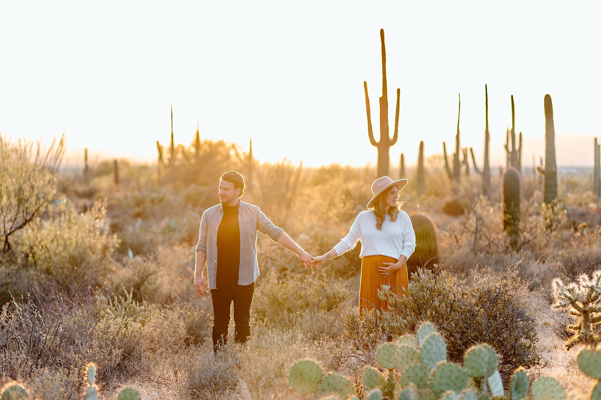  husband and wife hold hands in desert brush at Gates Pass session 
