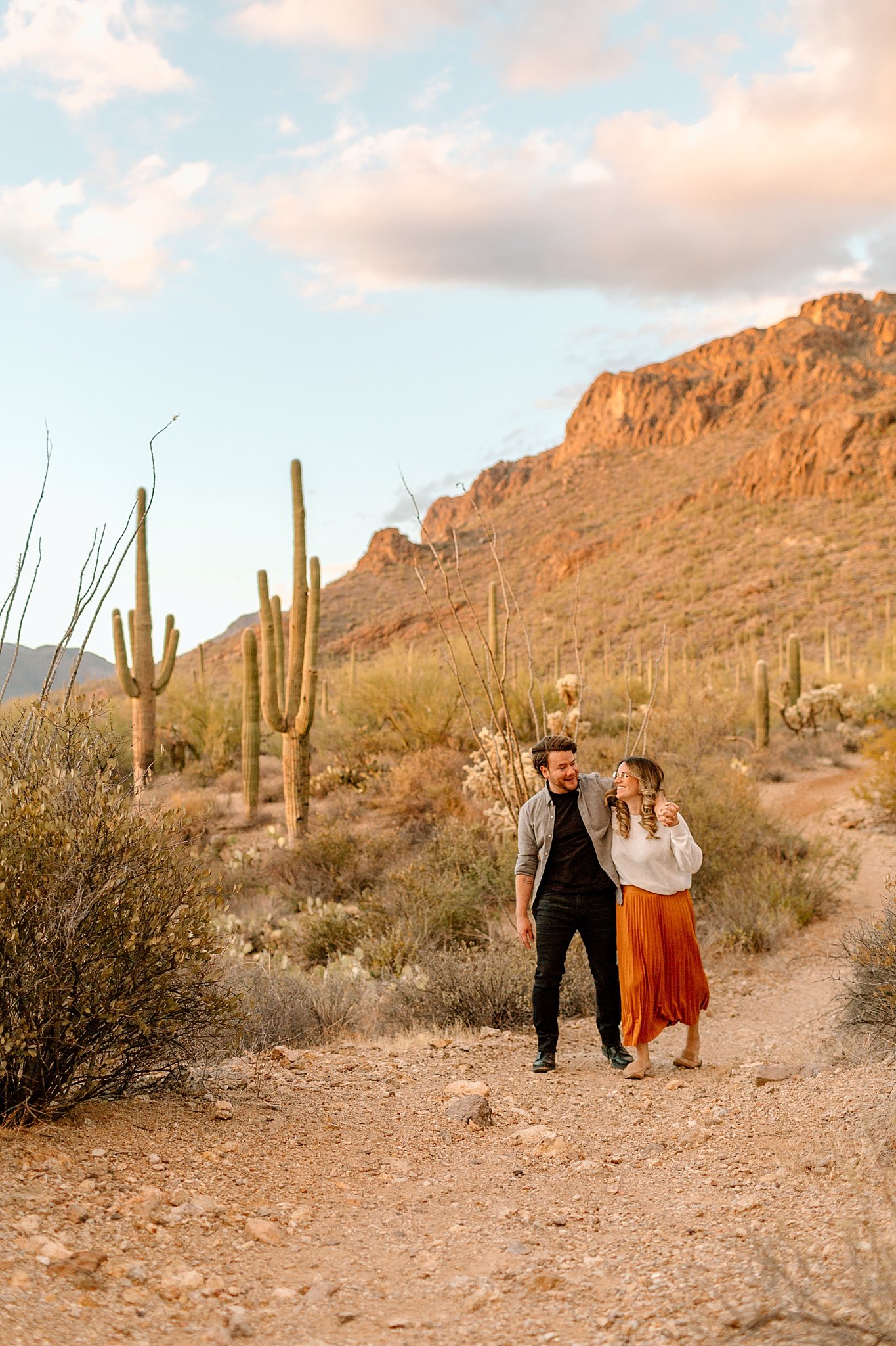  husband and wife walk closely together on dirt path in desert during Gates Pass session 