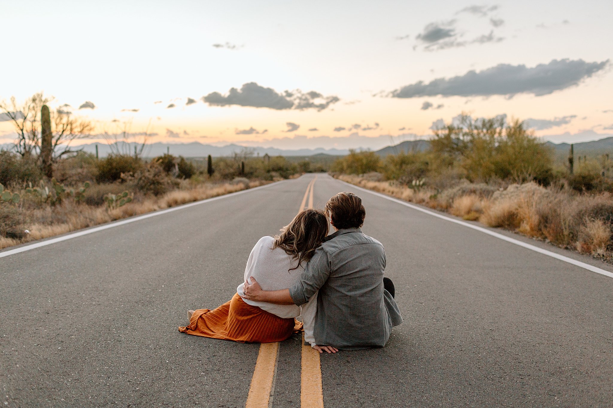  husband and wife sit on road overlooking sunset at Gates Pass session 