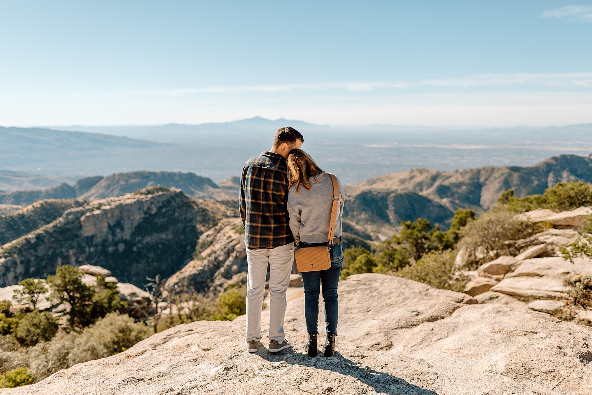  couple leans together while looking out over desert by Arizona engagement photographer 