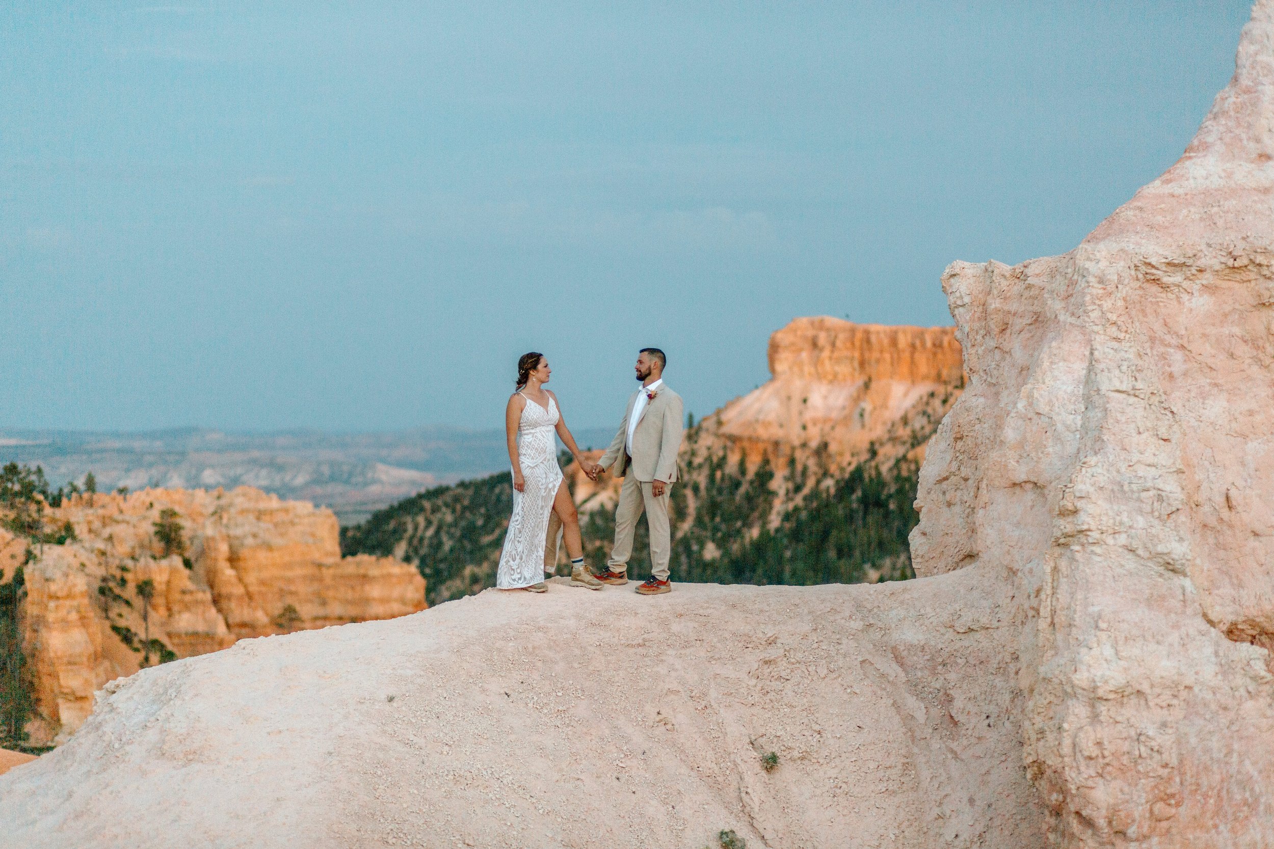  couple looks at each other while standing on a cliff edge by utah elopement photographer 