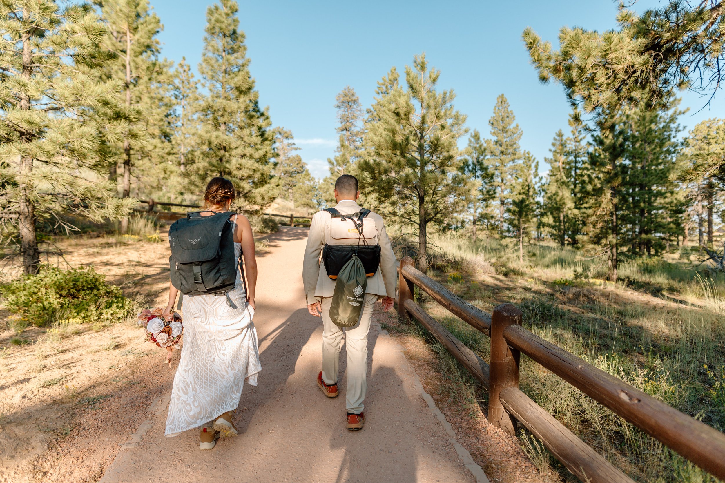  elopement couple wearing backpacks hikes through forest at bryce canyon national park 