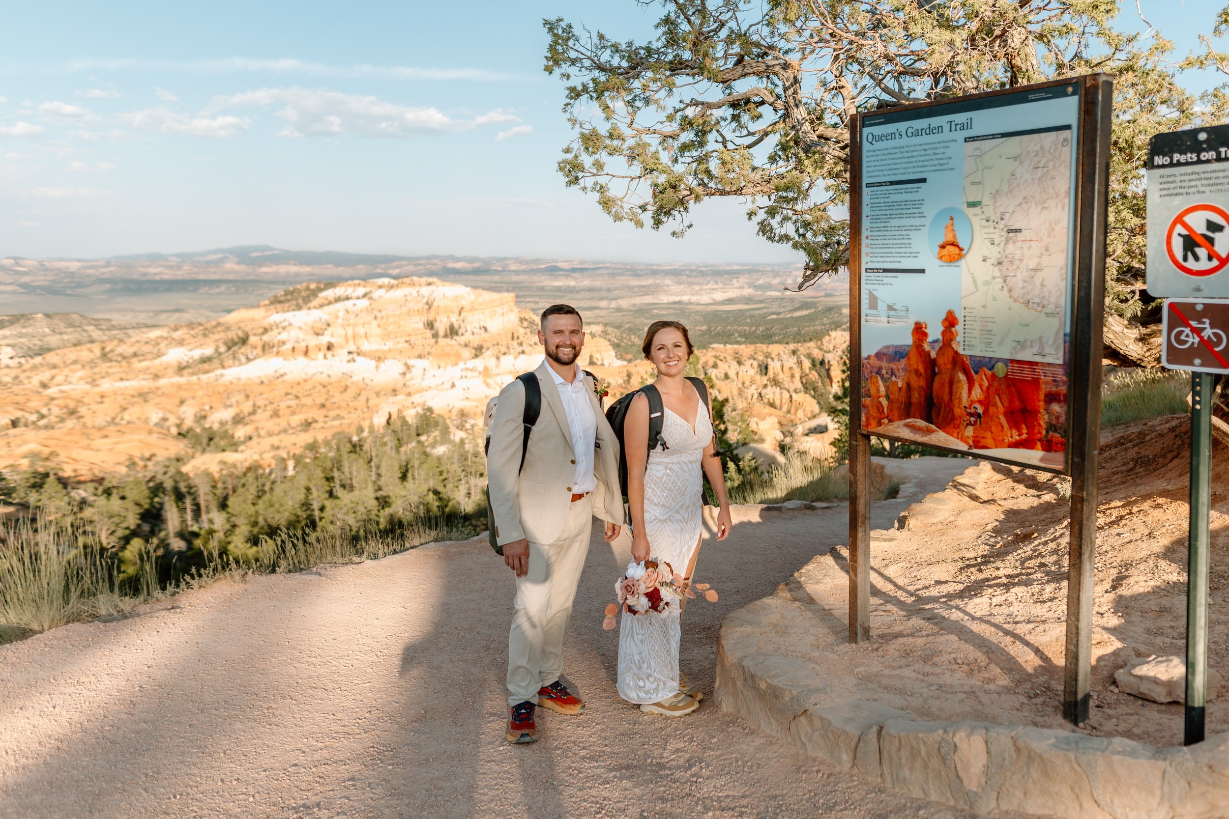  bryce canyon elopement couple smiles next to queen’s garden trail sign 