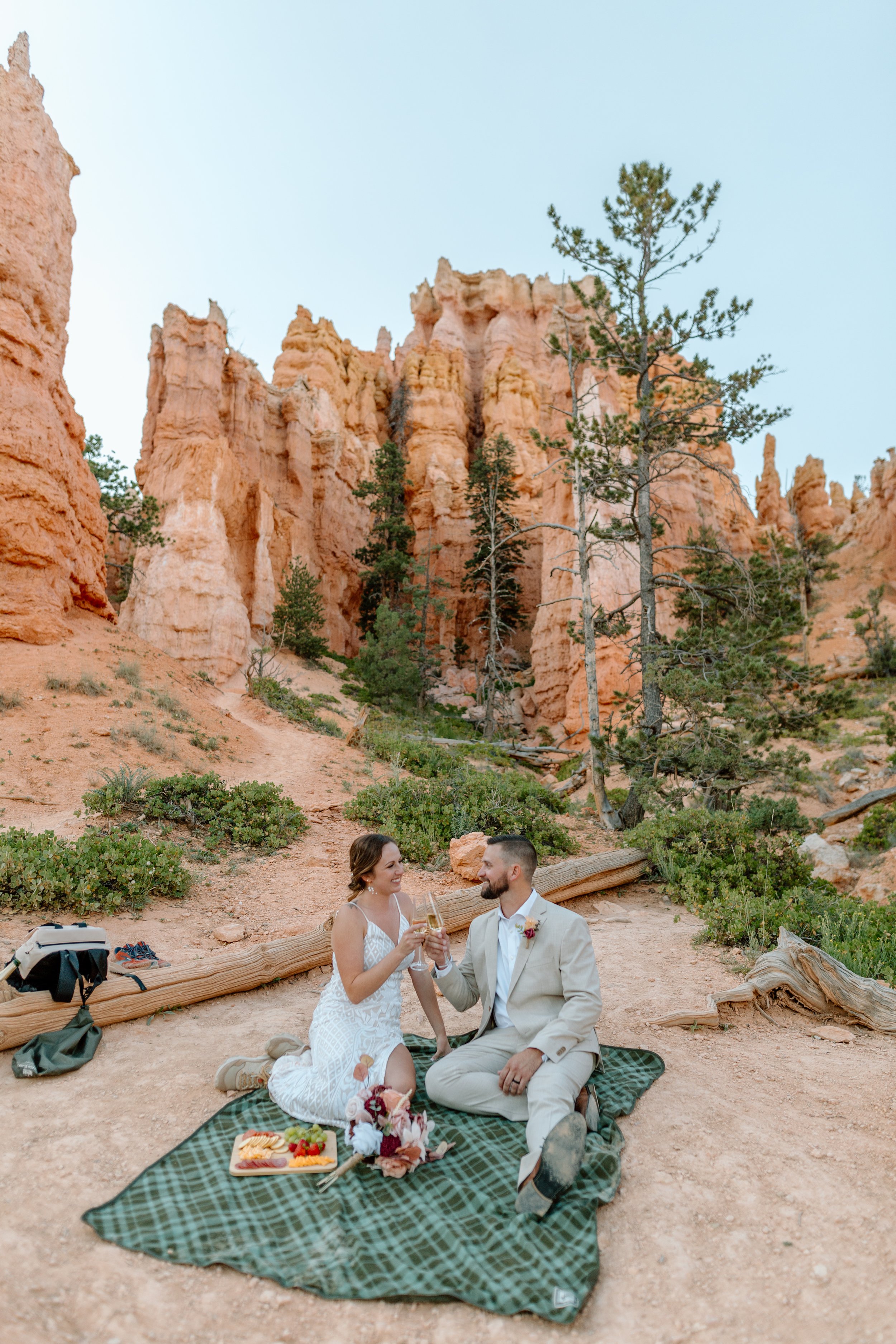  utah elopement couple clinks champagne glasses on picnic blanket at bryce canyon national park 