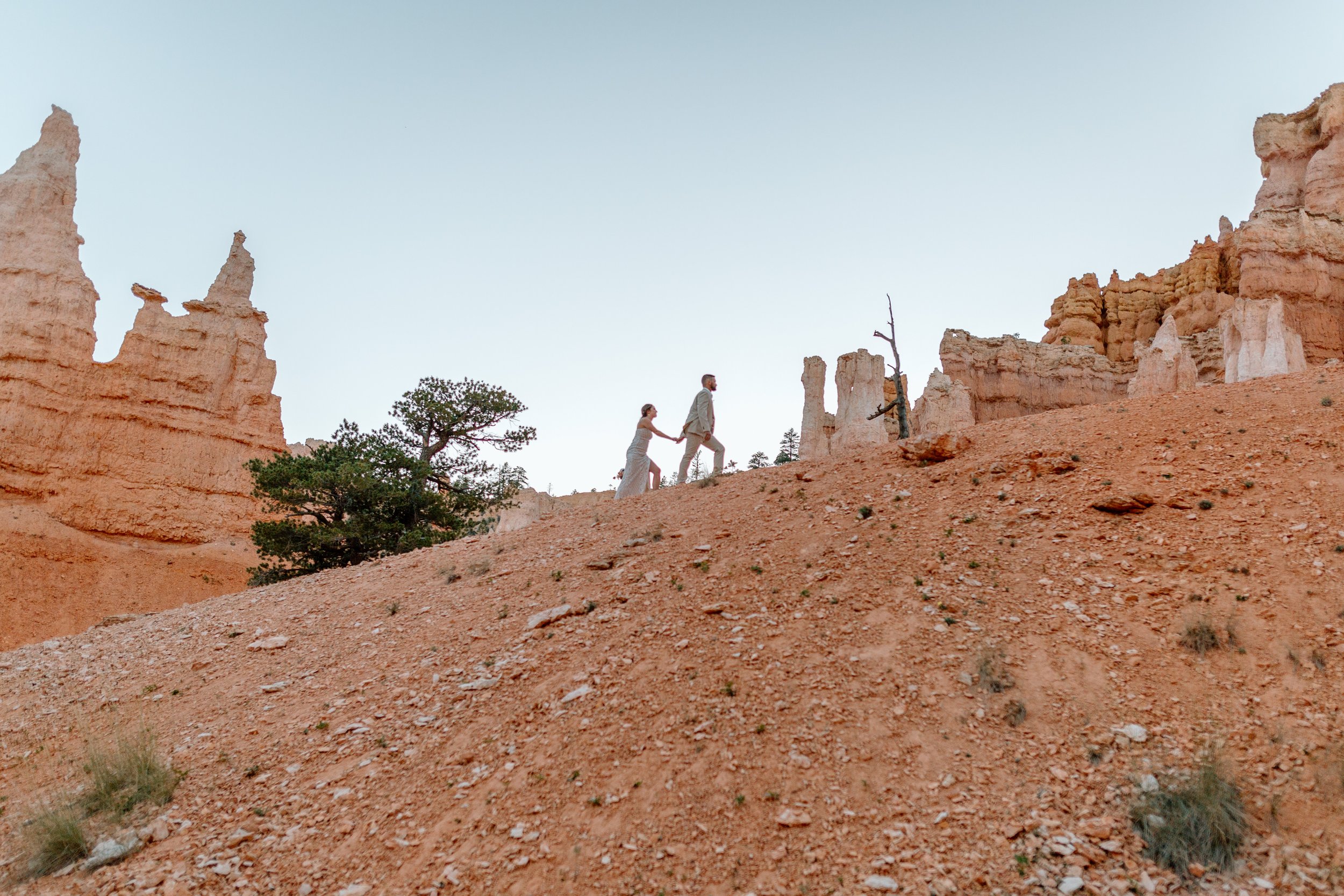  couple holds hands and walks uphill by bryce canyon elopement photographer 