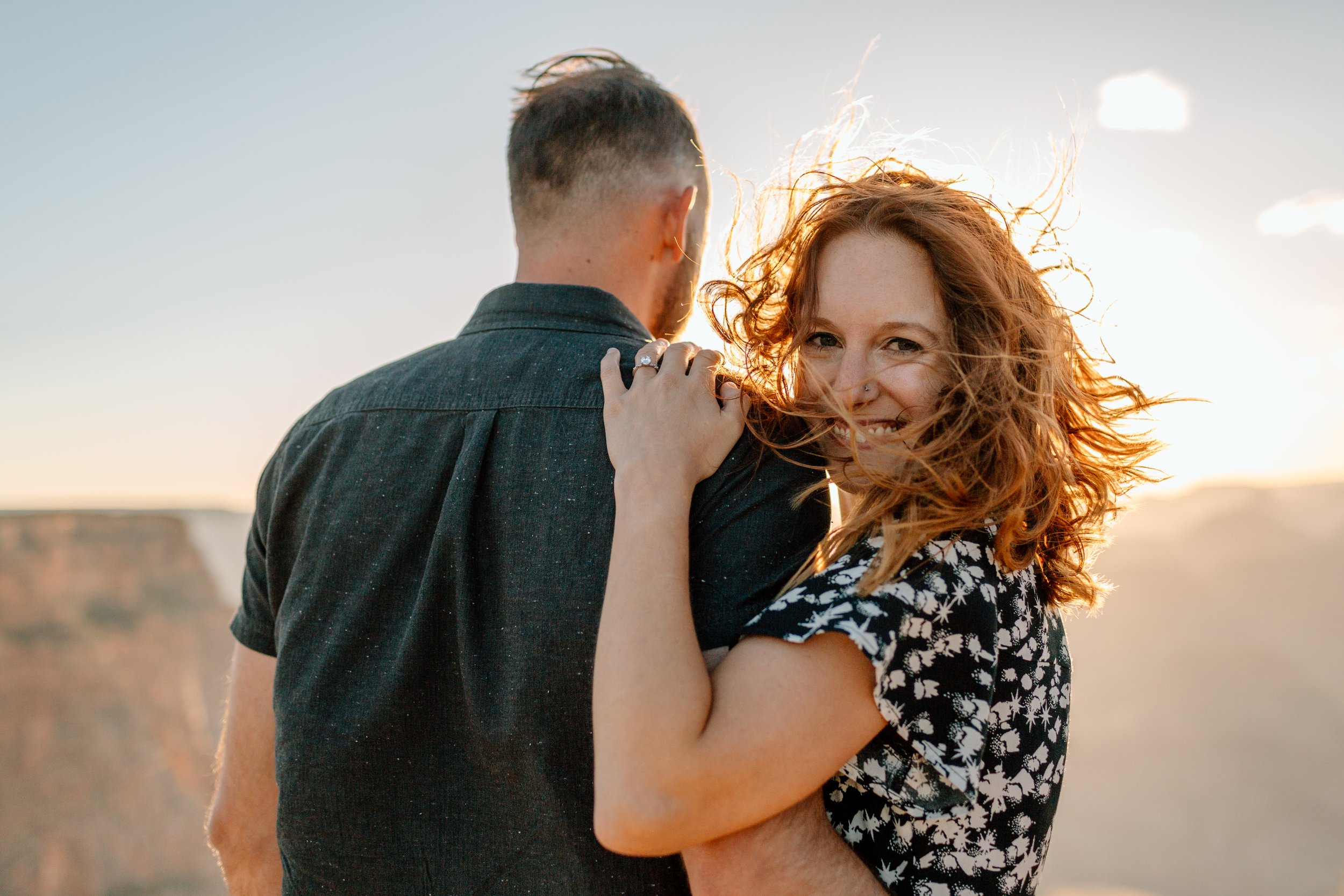  woman smiles at camera while holding onto her fiance during their arizona engagement session 