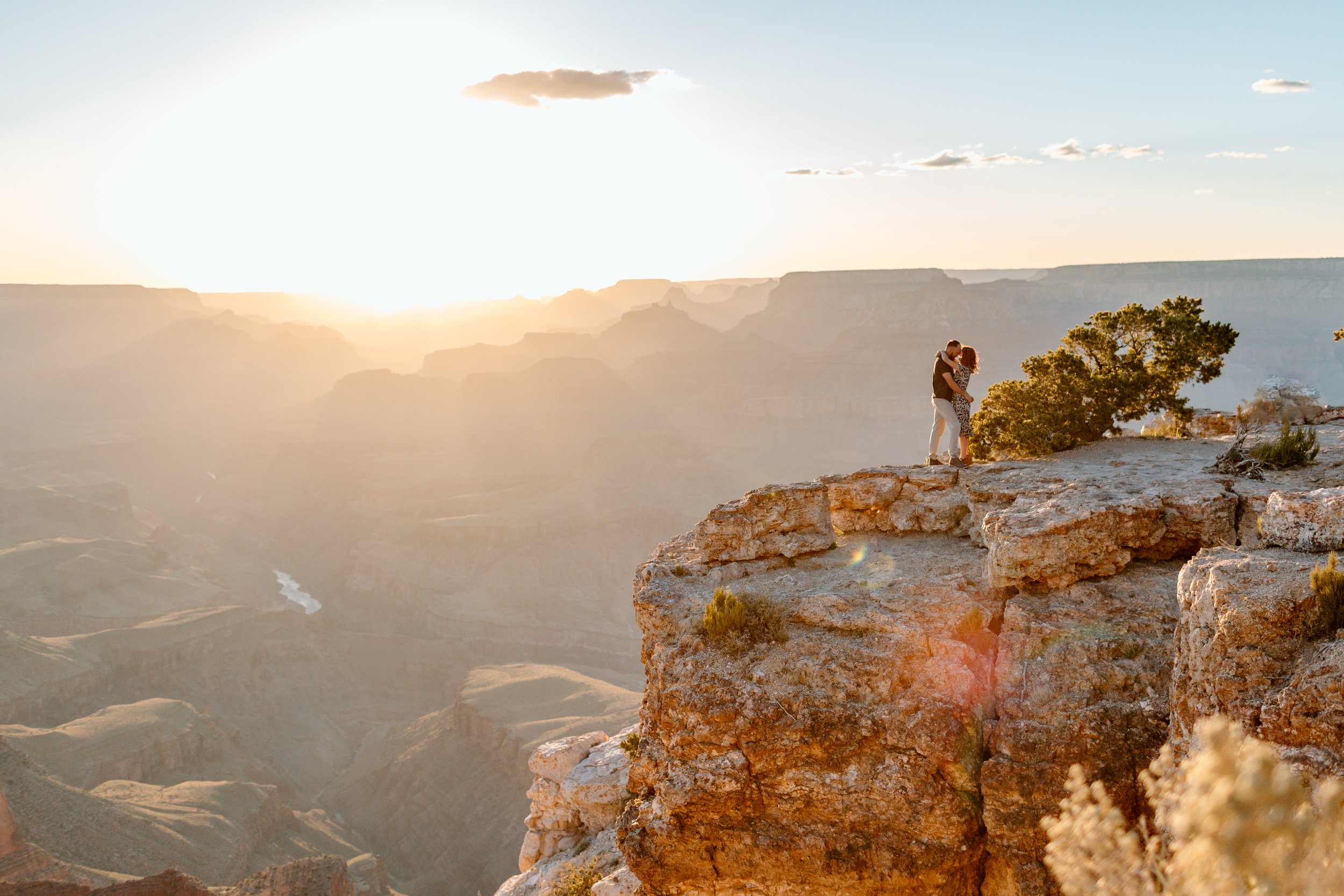  wide view of a grand canyon sunset and couple kissing in the distance during their engagement session 