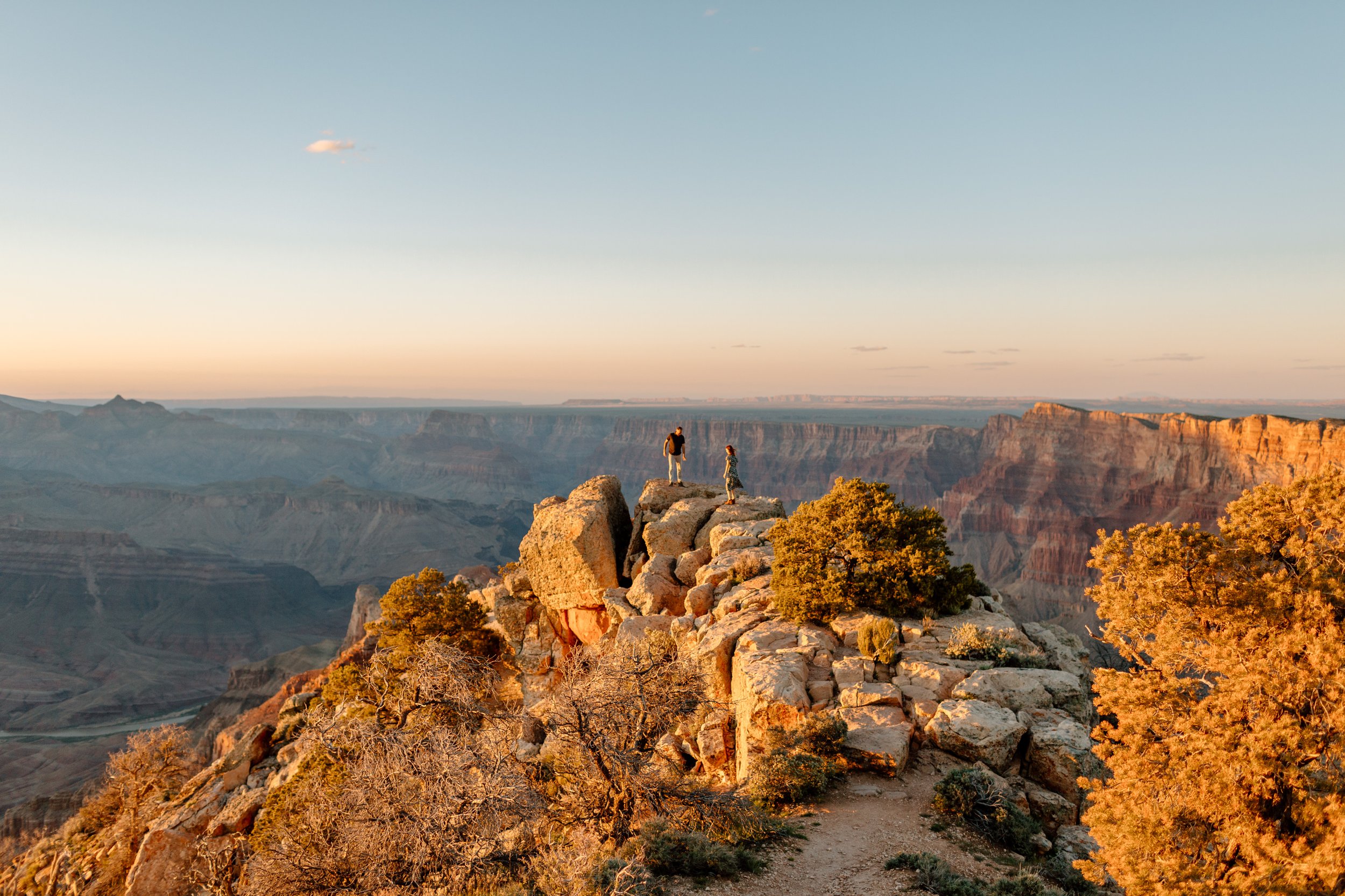  couple in distance scrambles on rocks for their grand canyon engagement session 