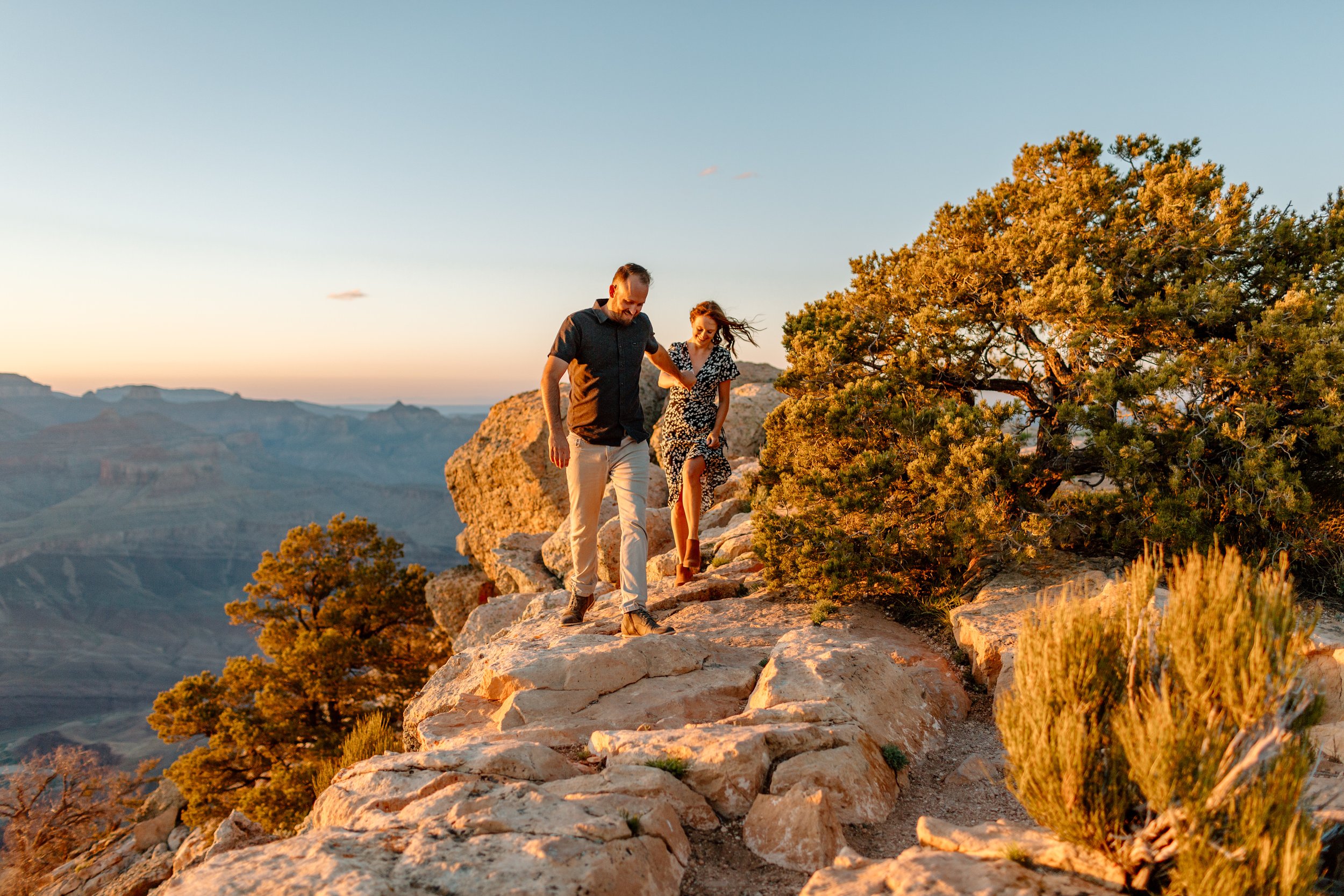  couple holds hands and walks down rocks during grand canyon engagement session 
