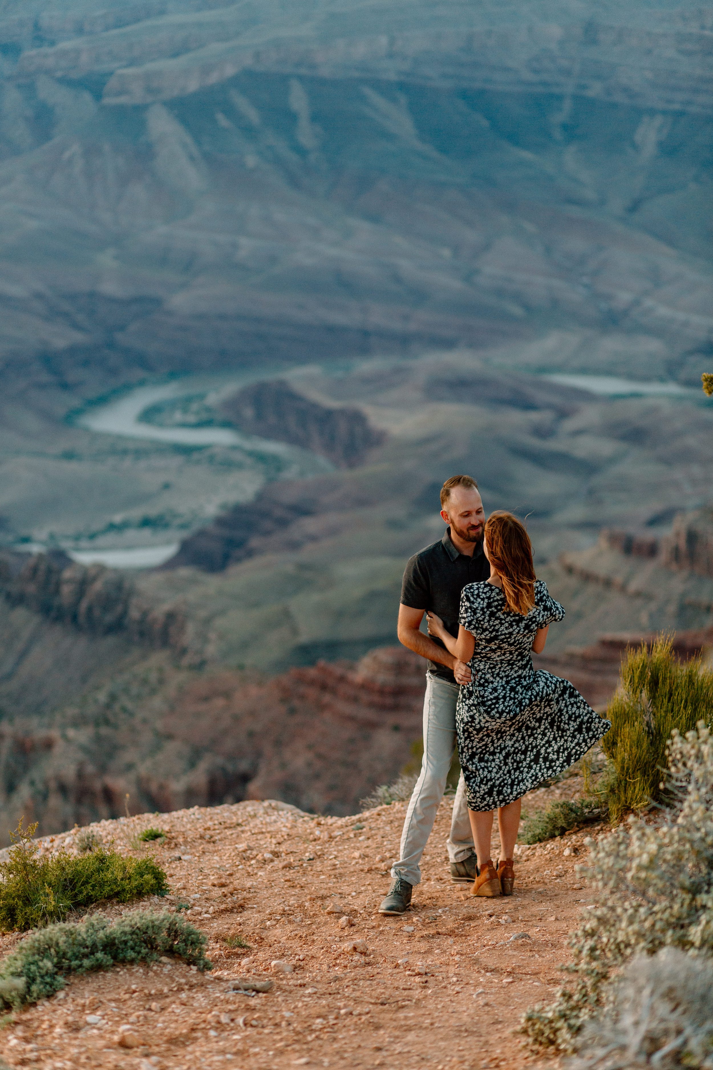  couple holds each other with colorado river at the bottom of the grand canyon in the background 