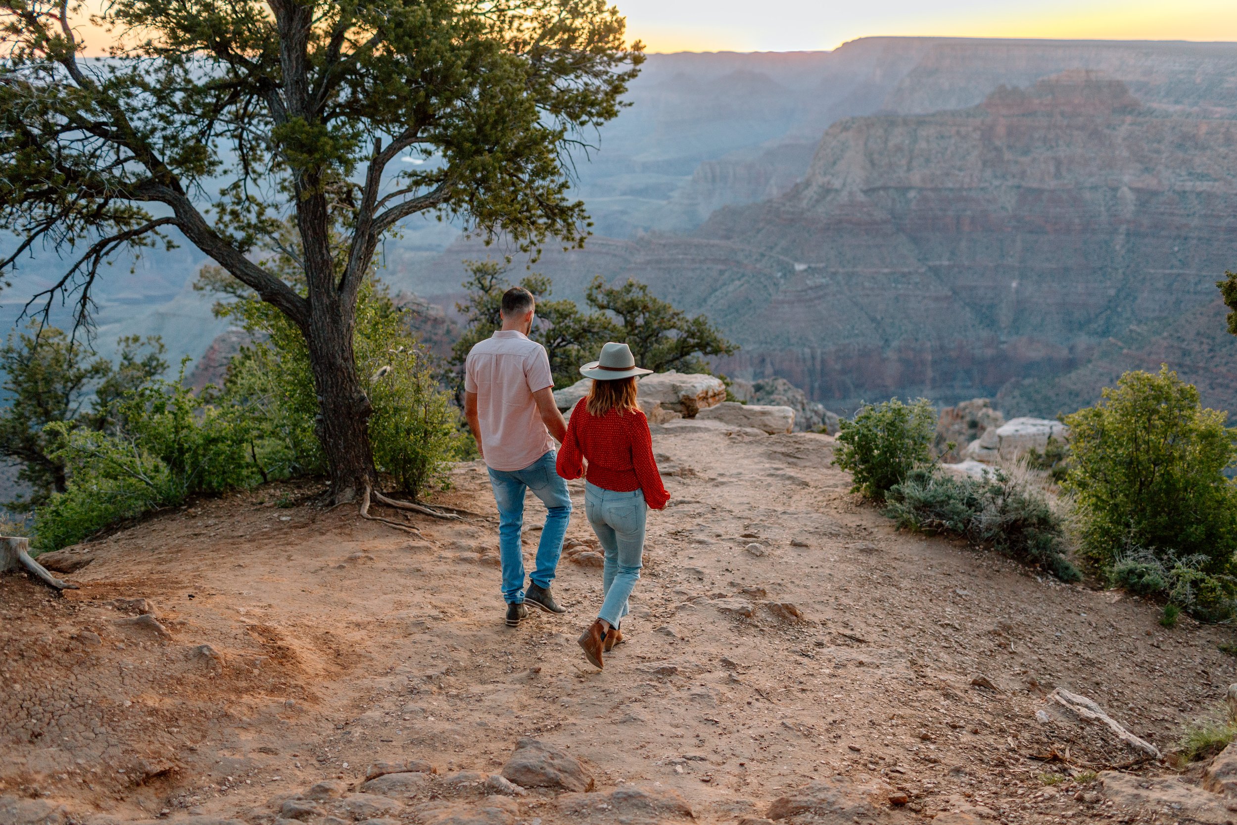  couple holds hands and walks together towards the south rim of the grand canyon 