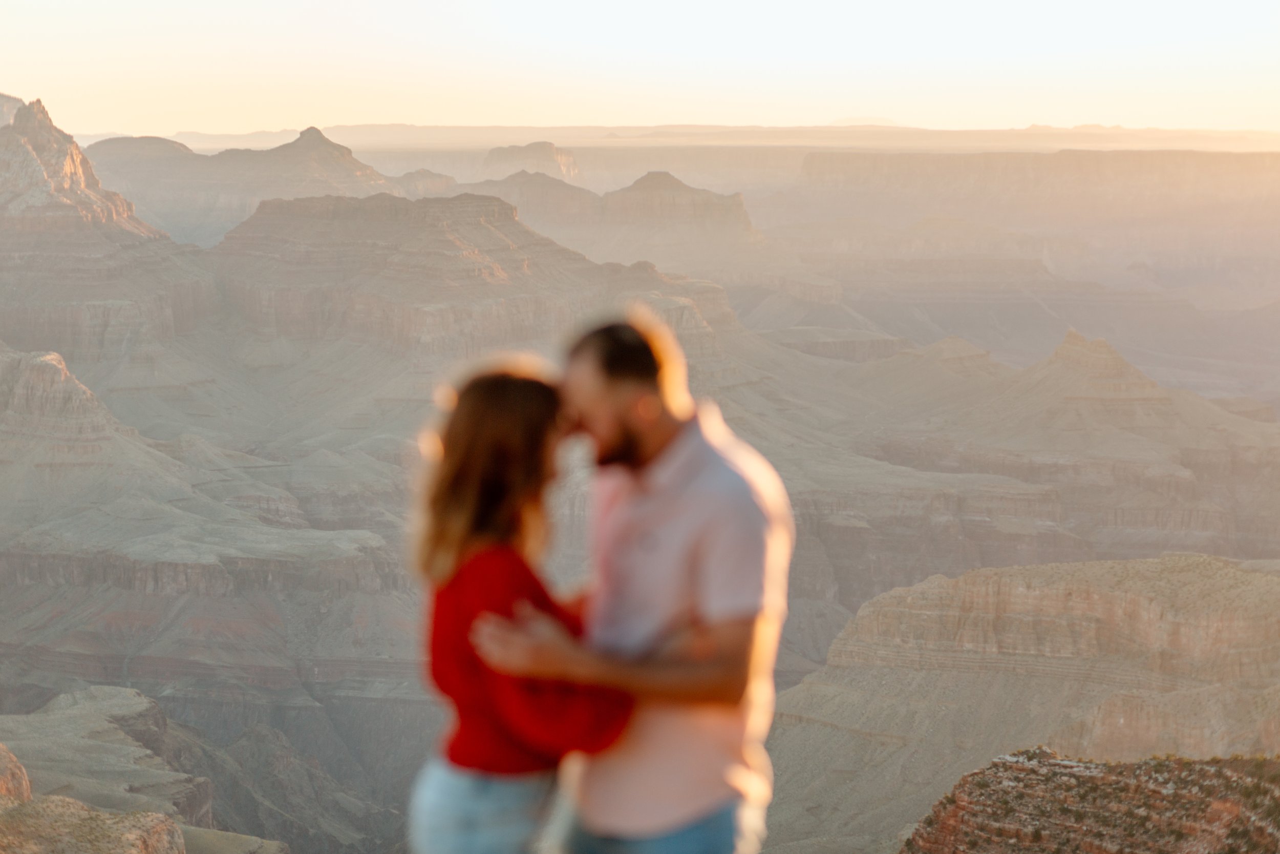  blurry couple holds each other with grand canyon in focus in the background 