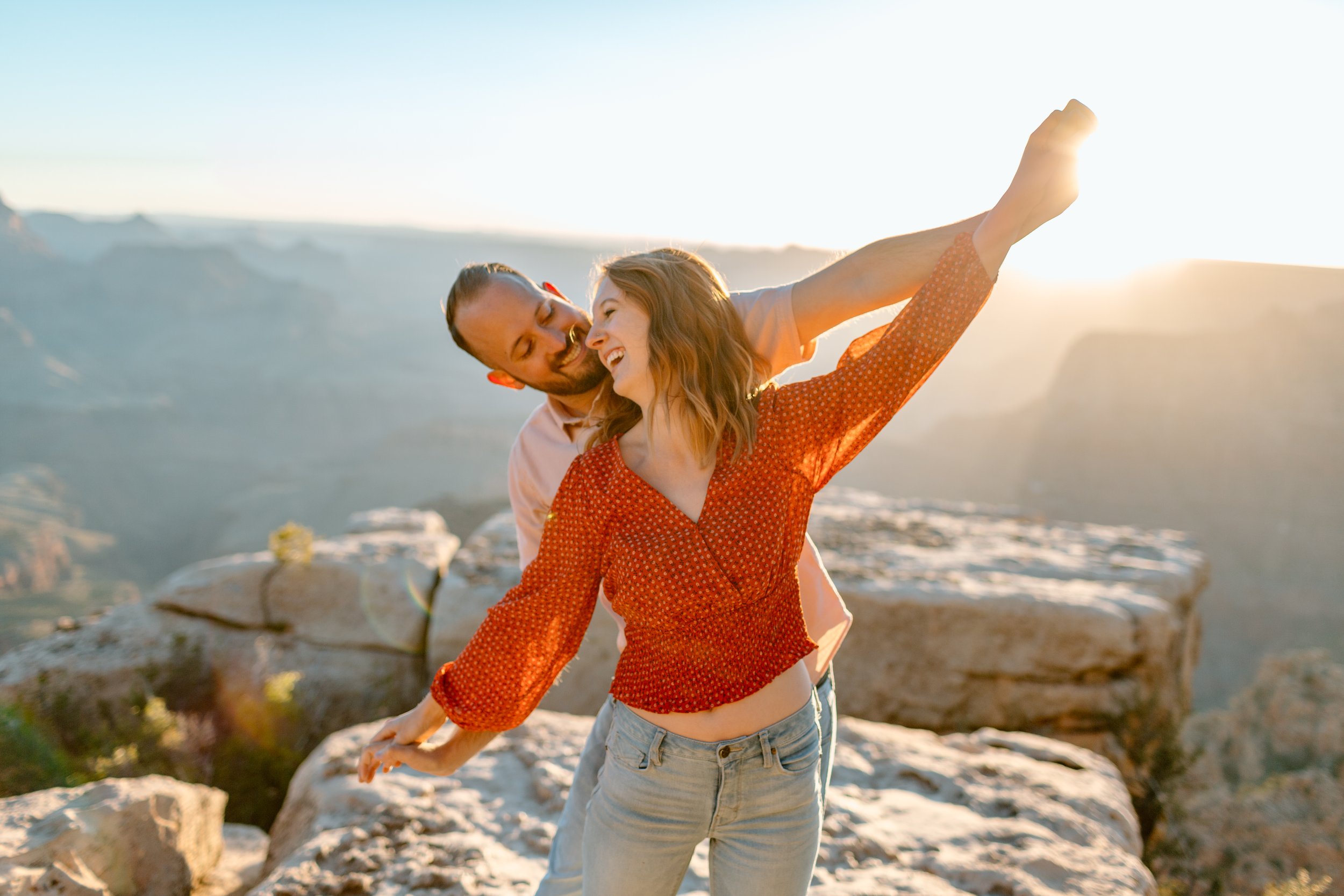  arizona engagement couple holds their arms out together and laughs at the grand canyon 