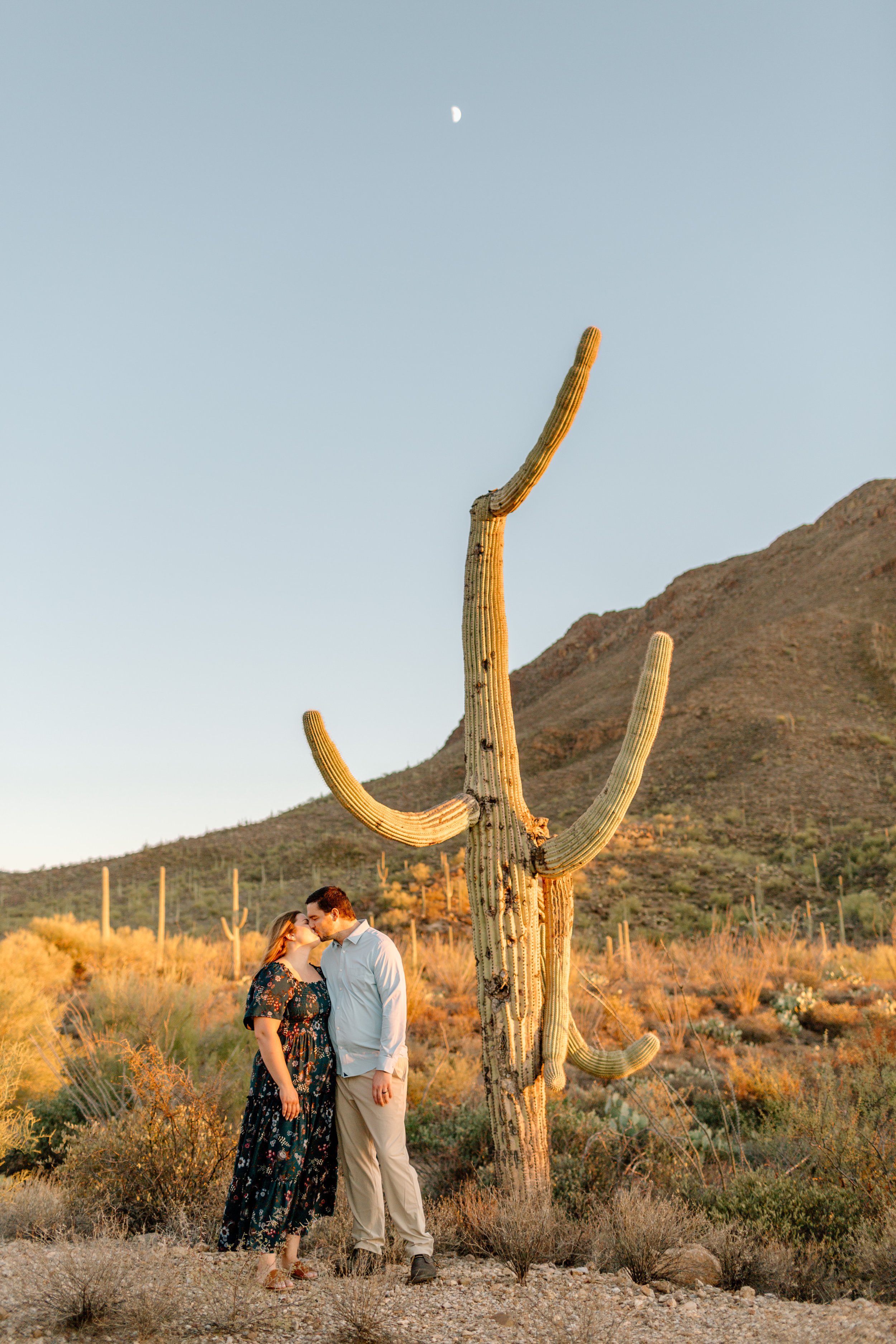  couple kisses under a saguaro cactus and the rising moon during their arizona engagement session 