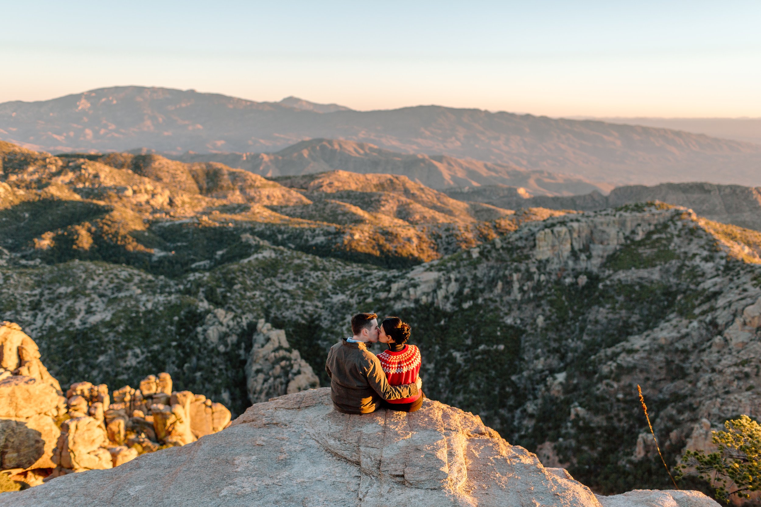  couple sits on a ledge and kisses overlooking mount lemmon in tucson arizona 