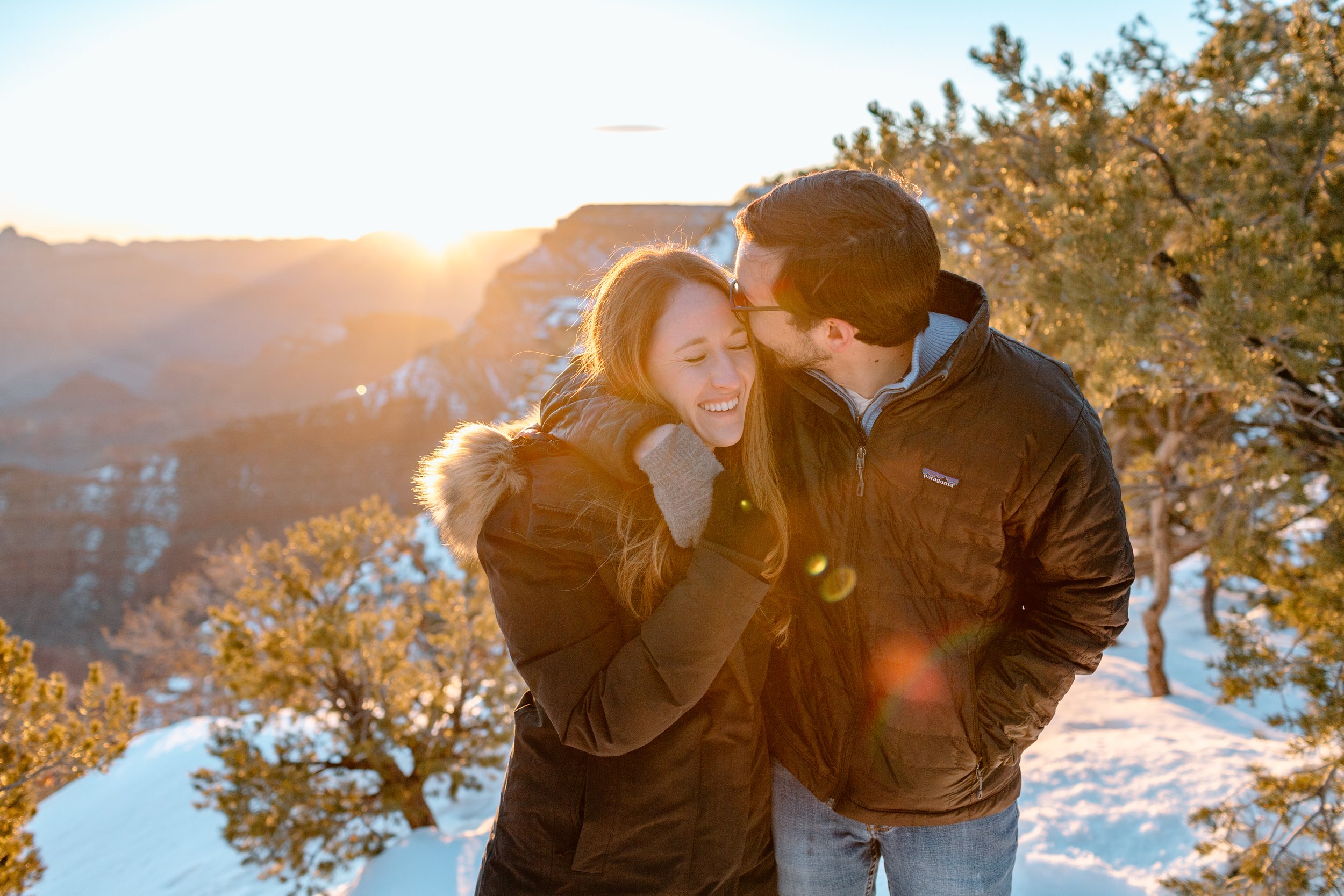  man kisses his fiance on her forehead as they snuggle during a grand canyon sunrise 