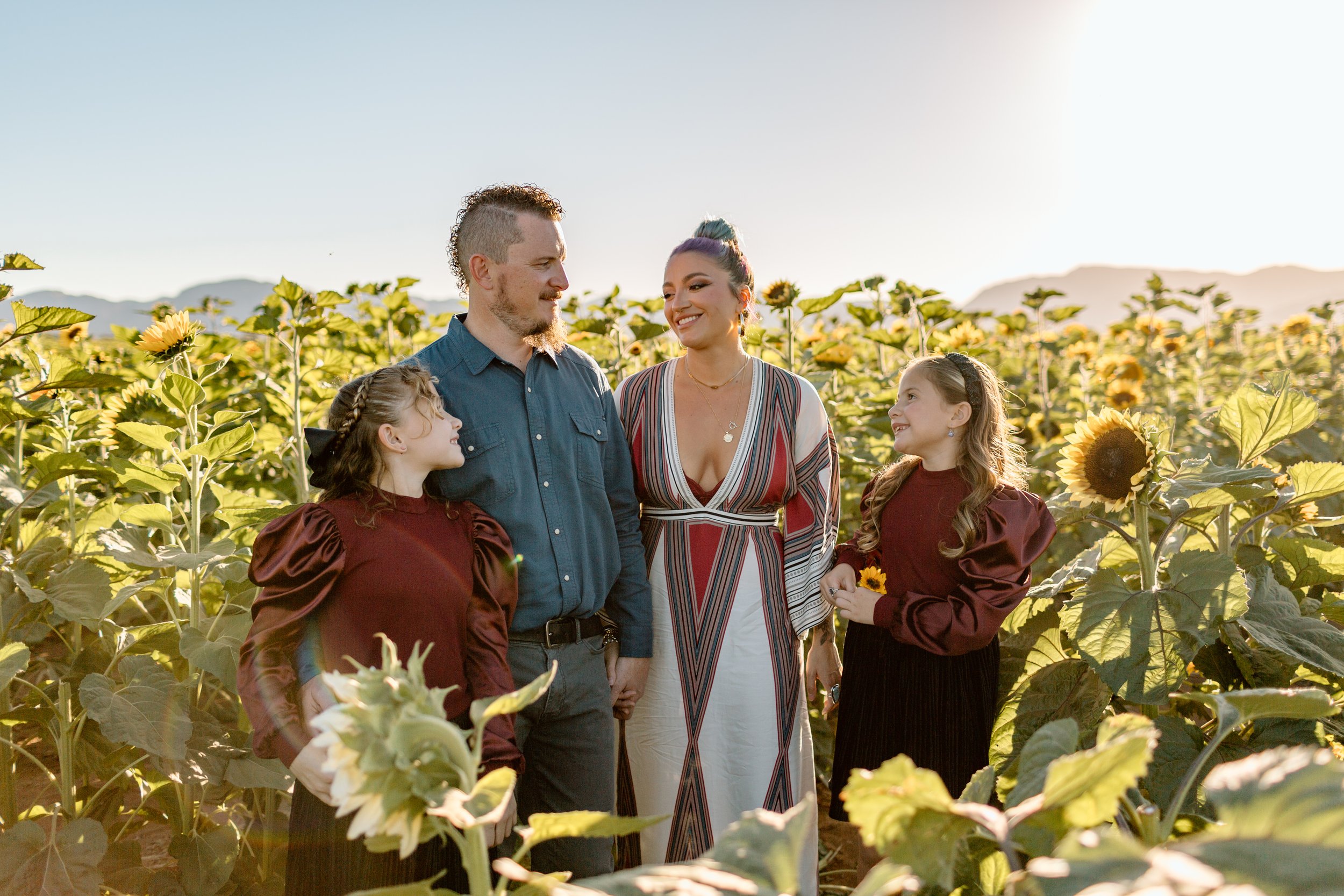  parents and two daughters smile at each other in a field of sunflowers 