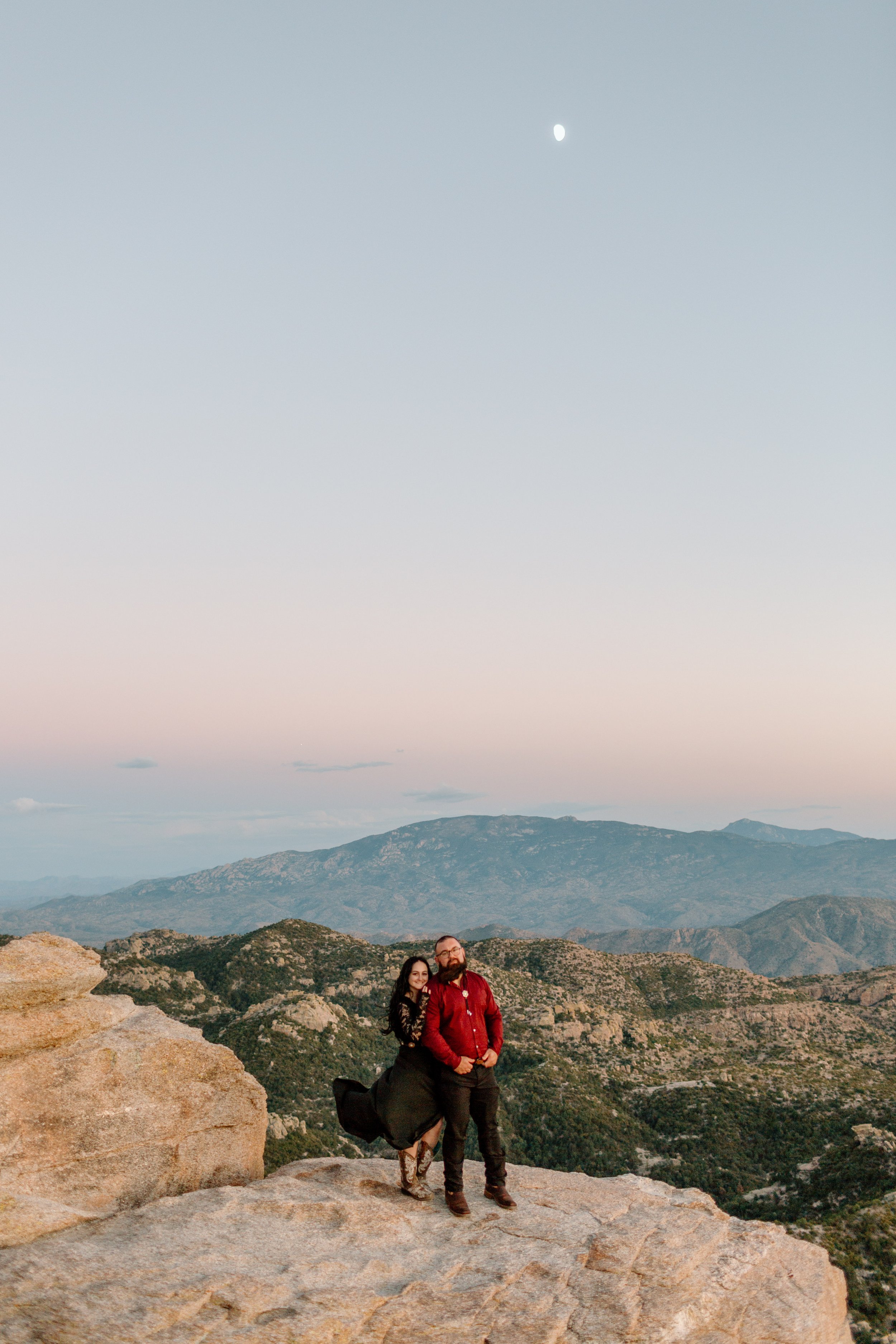  wide shot of mountains with couple smiling for the camera with wind blowing the woman’s dress 