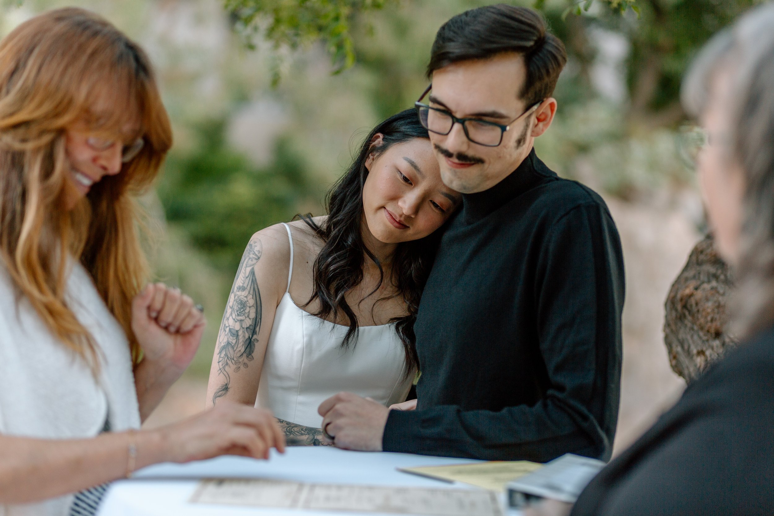  couple cuddles while watching family member sign their marriage license during their arizona elopement 