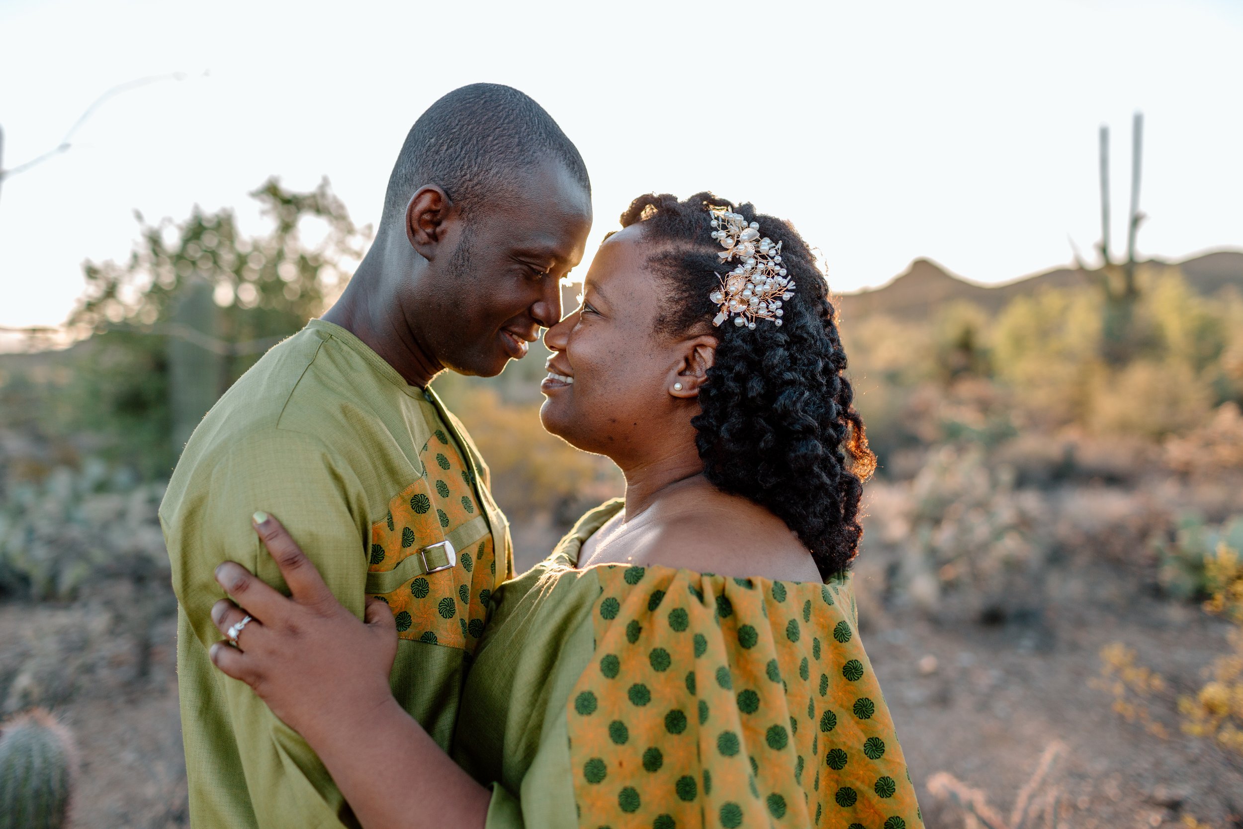  couple smiles with faces close to each other as sun rises behind them in the sonoran desert 