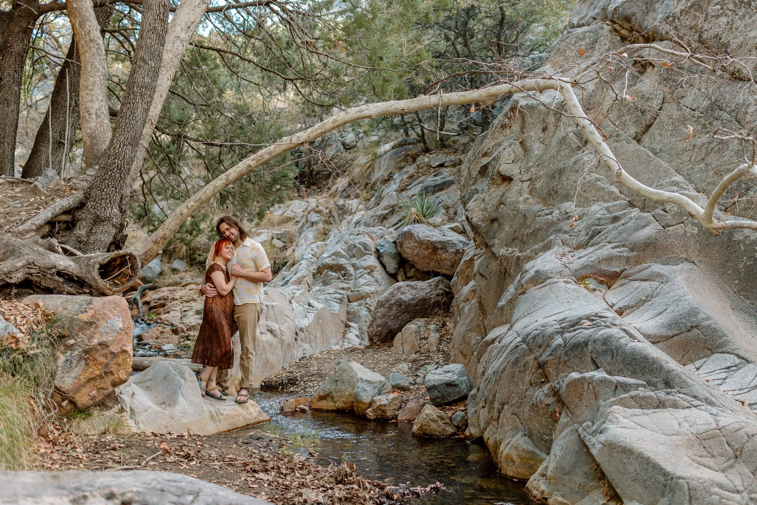  couple snuggles while standing on rock in stream at Madera Canyon 