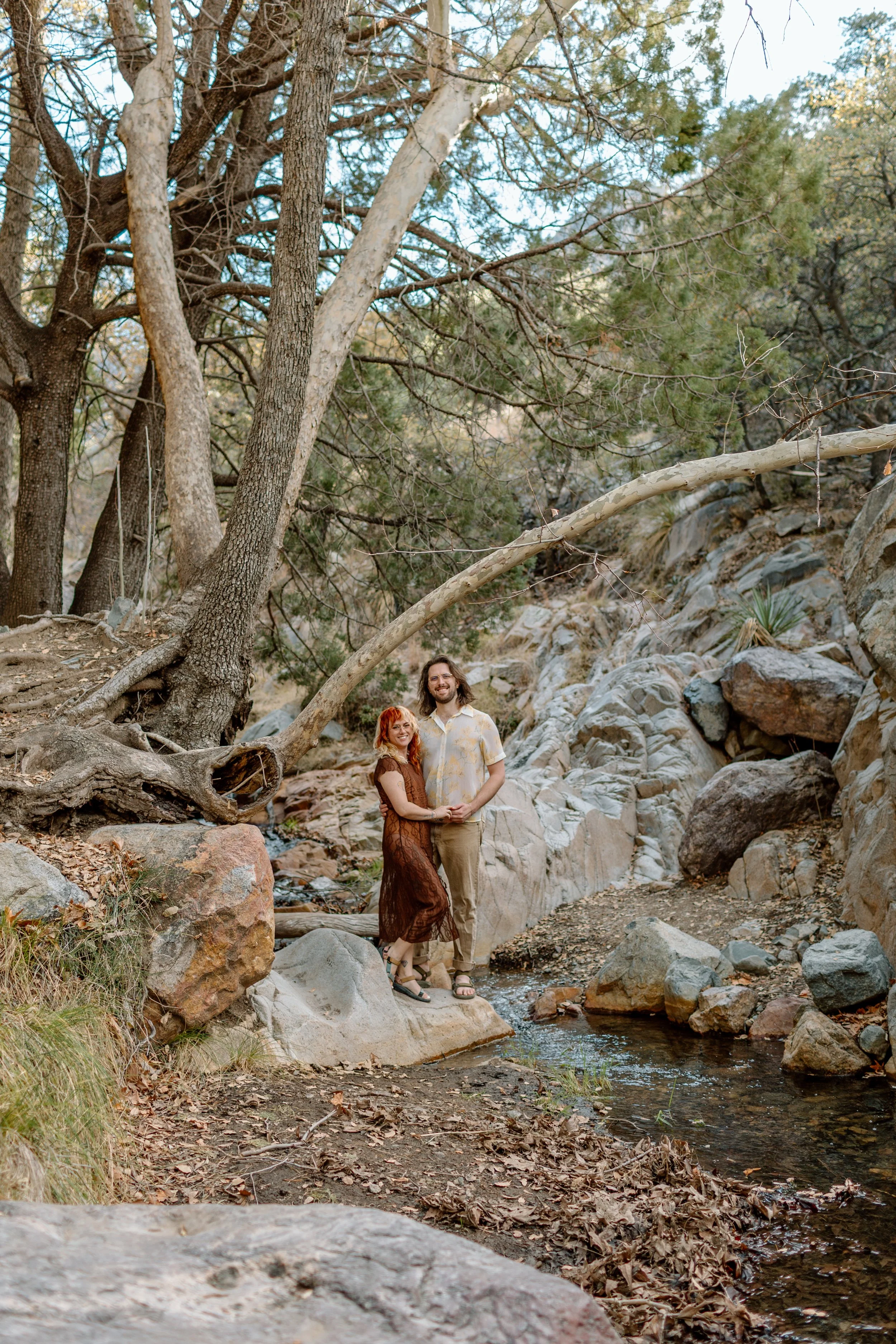  couple stands on rock in stream and smiles at camera during Tucson engagement session 