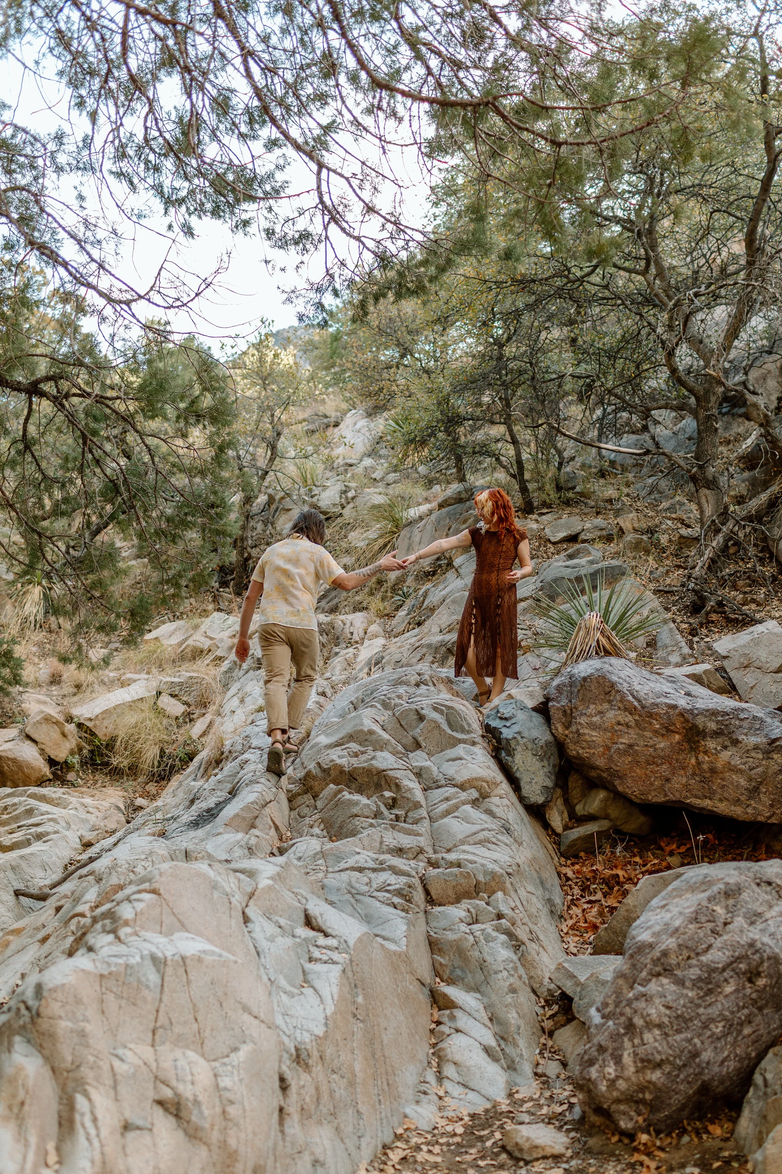  couple helps each other scramble up rocks during Madera Canyon engagement session 