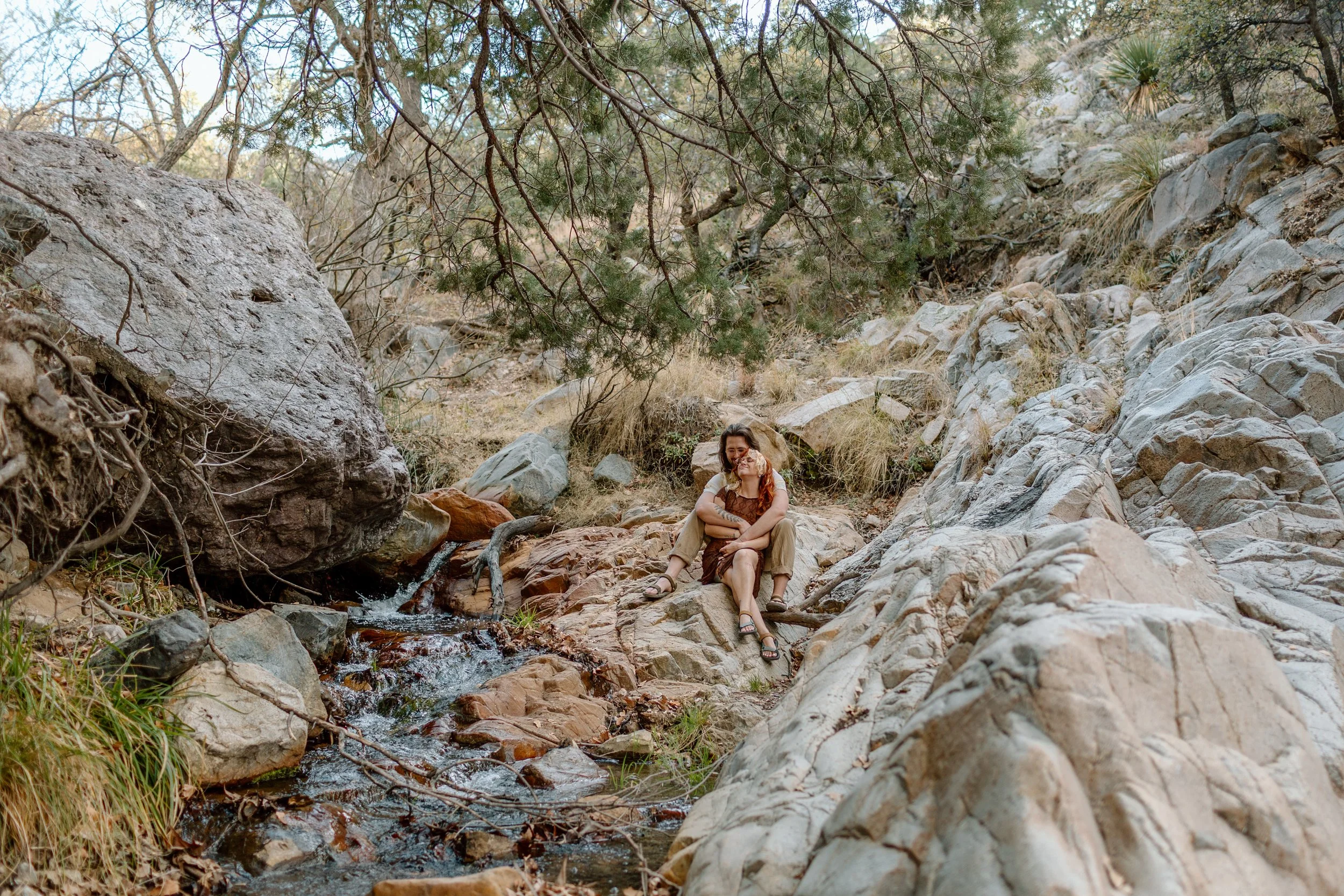  couple snuggles while sitting next to stream for Tucson engagement session 