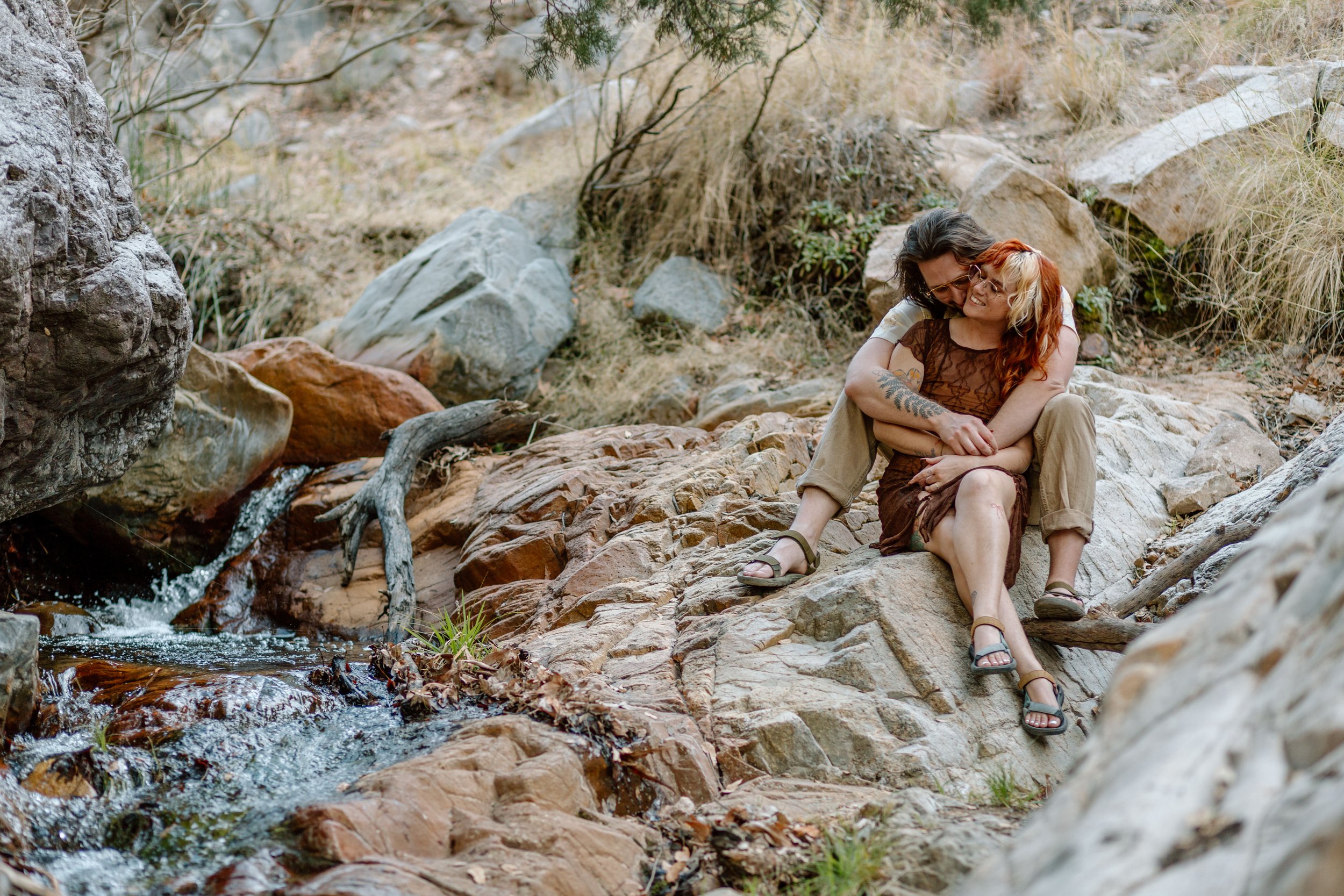  couple snuggles while sitting next to stream by Tucson engagement photographer 
