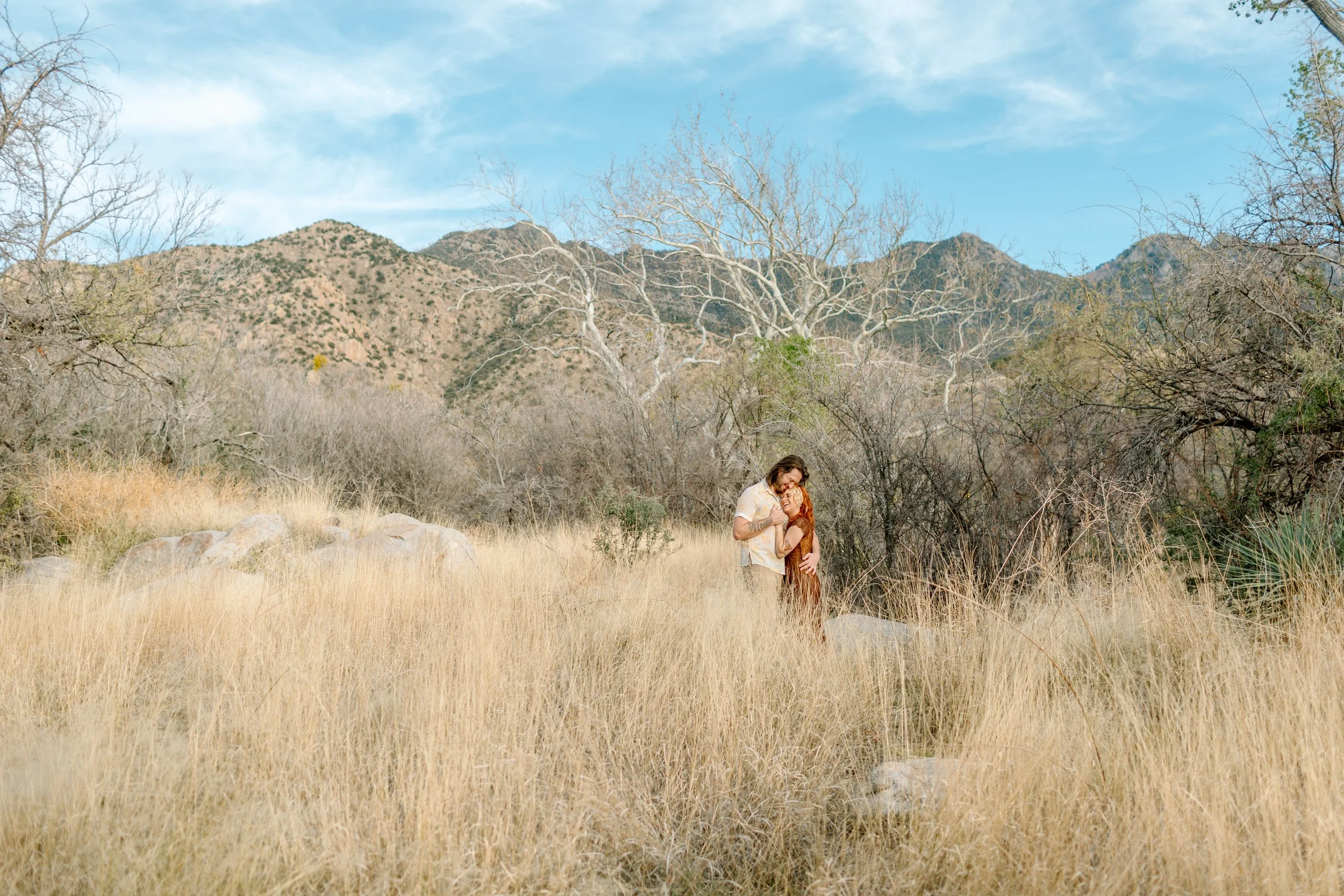  couple snuggles while standing in tall grass for Tucson engagement session 