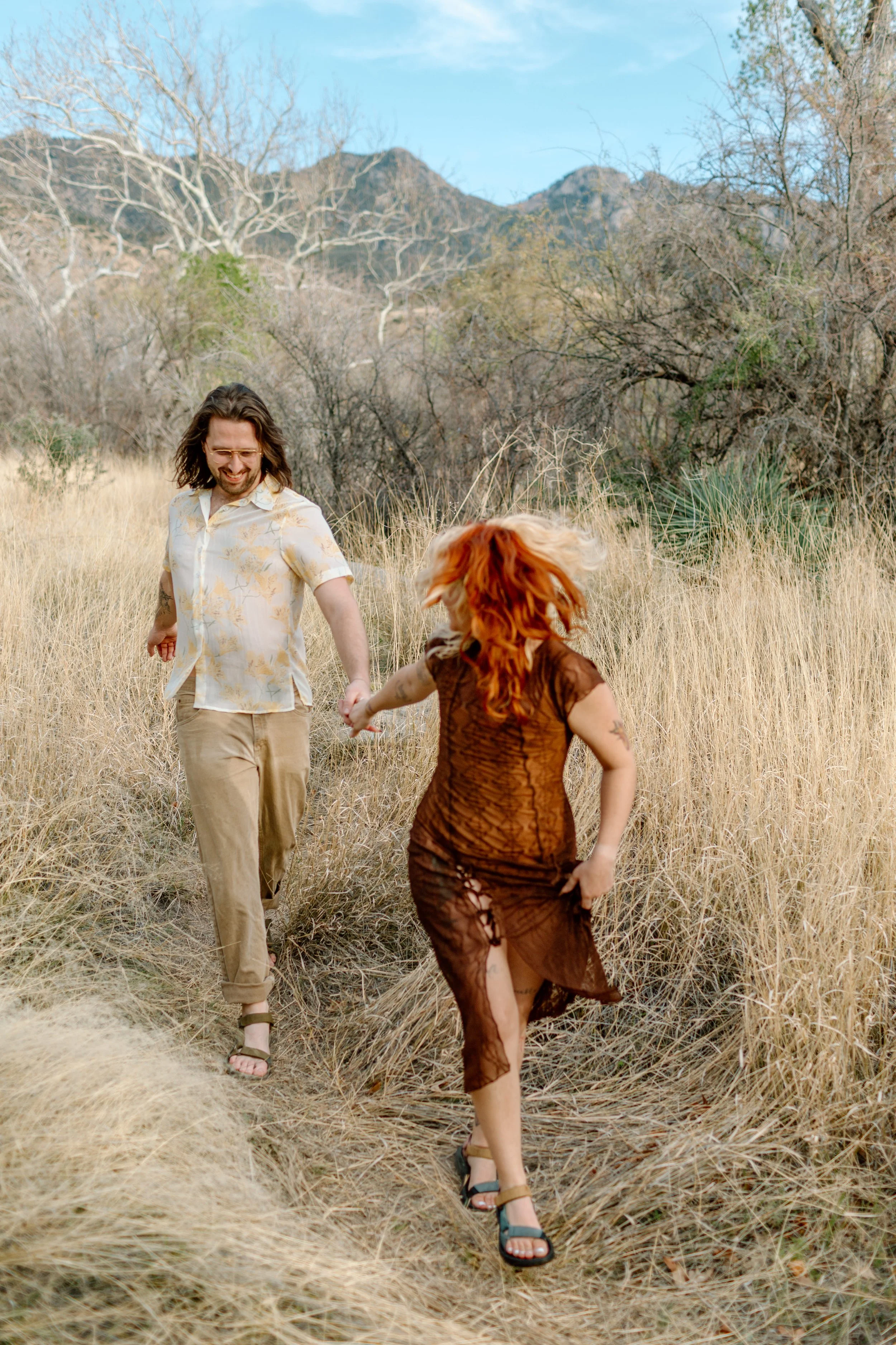  couple runs together out of tall grass during Madera Canyon engagement session 