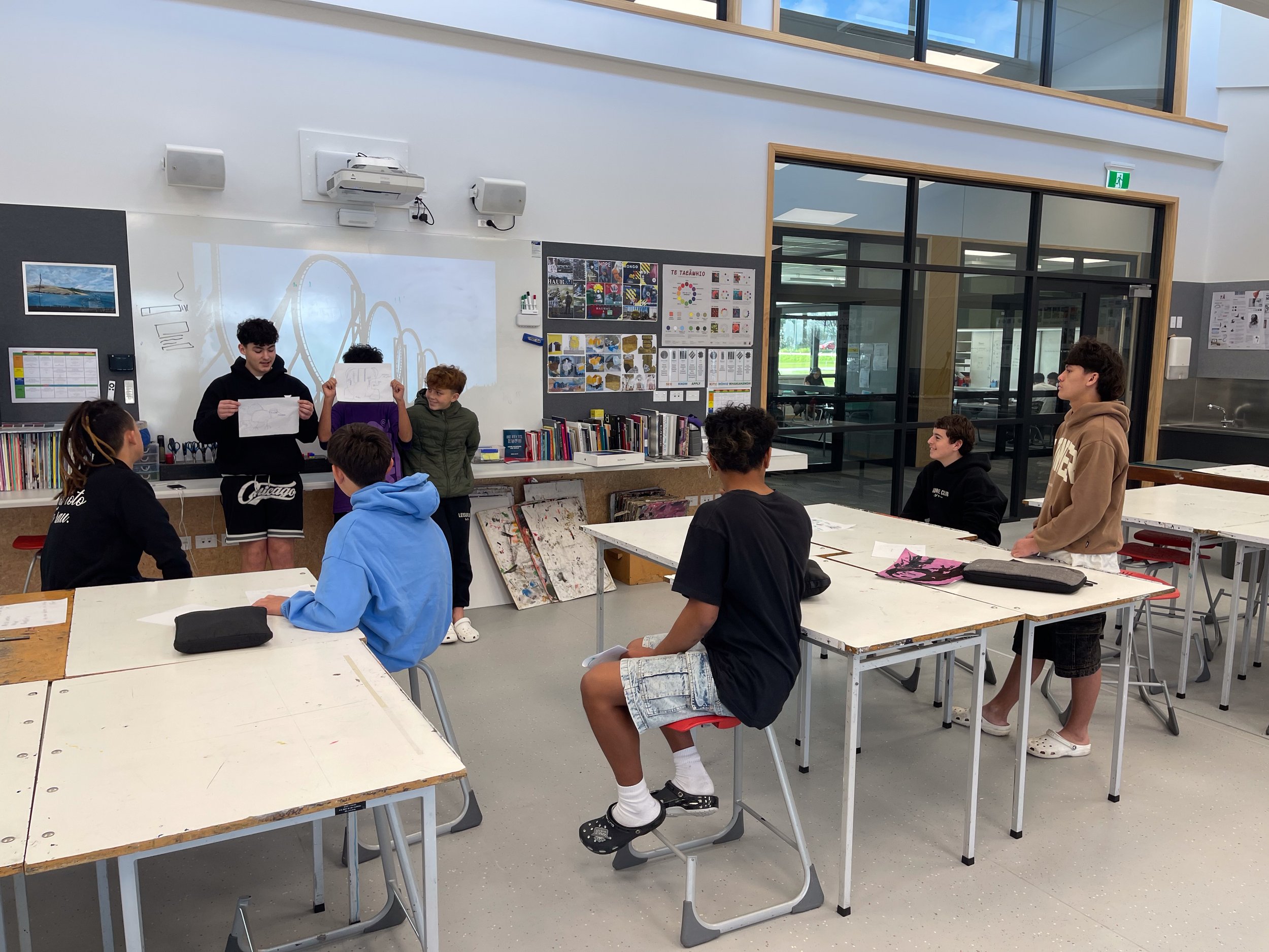 Students in a classroom presenting drawings on a whiteboard with roller coaster image