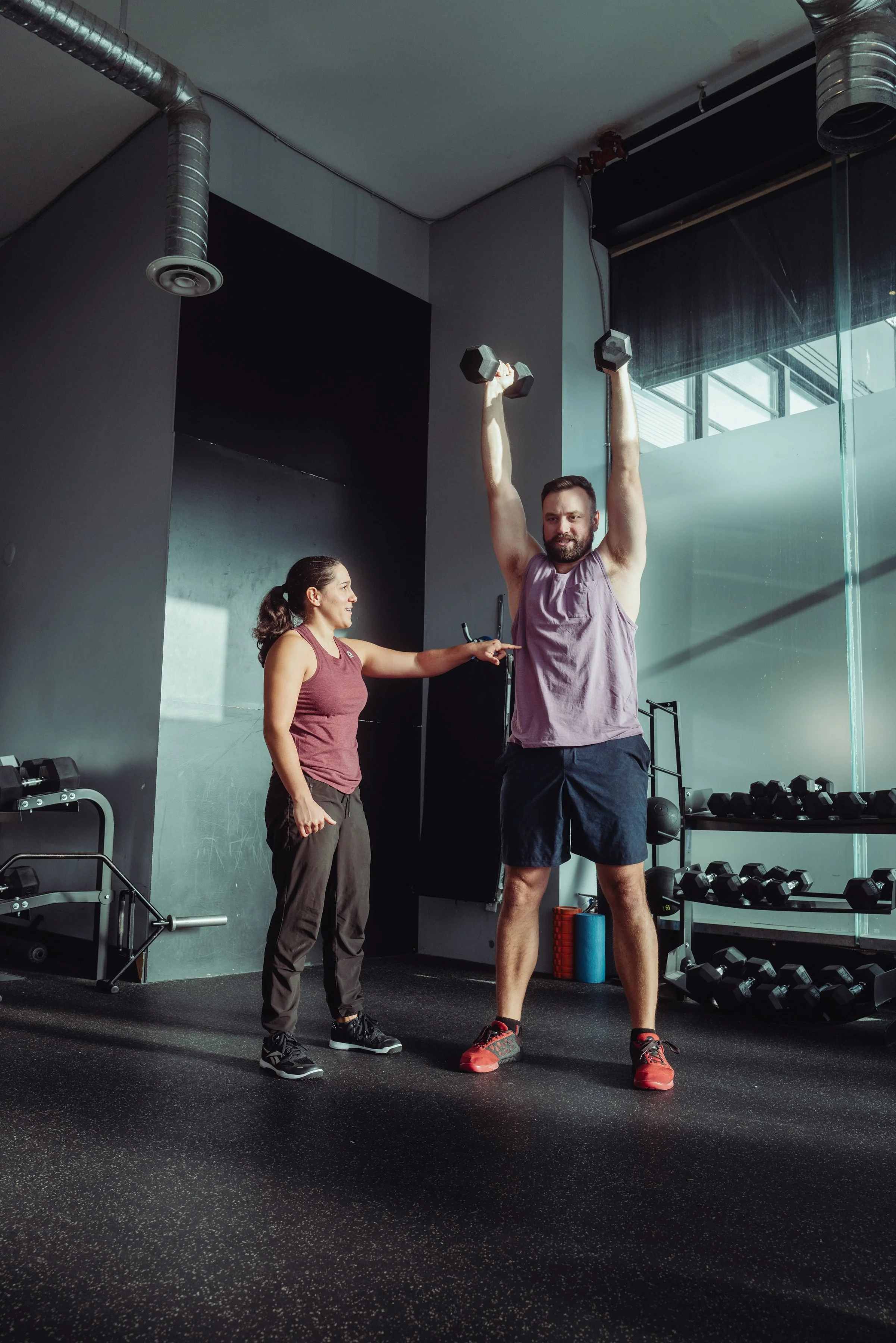 Personal trainer coaching a client's dumbbell overhead press form during a 1-on-1 training session in Vancouver