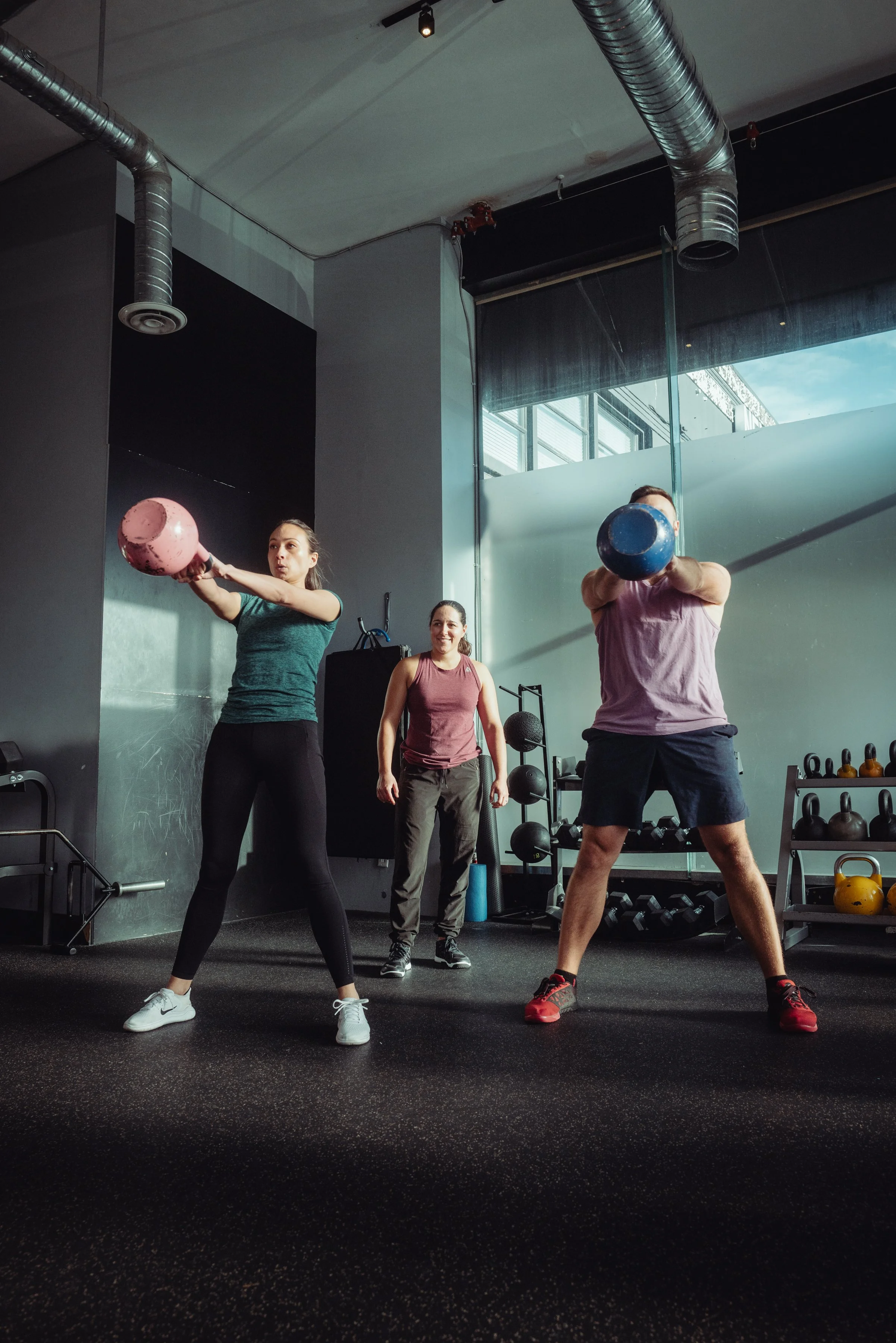 Coach supervising two clients performing kettlebell swings during group training in Vancouver