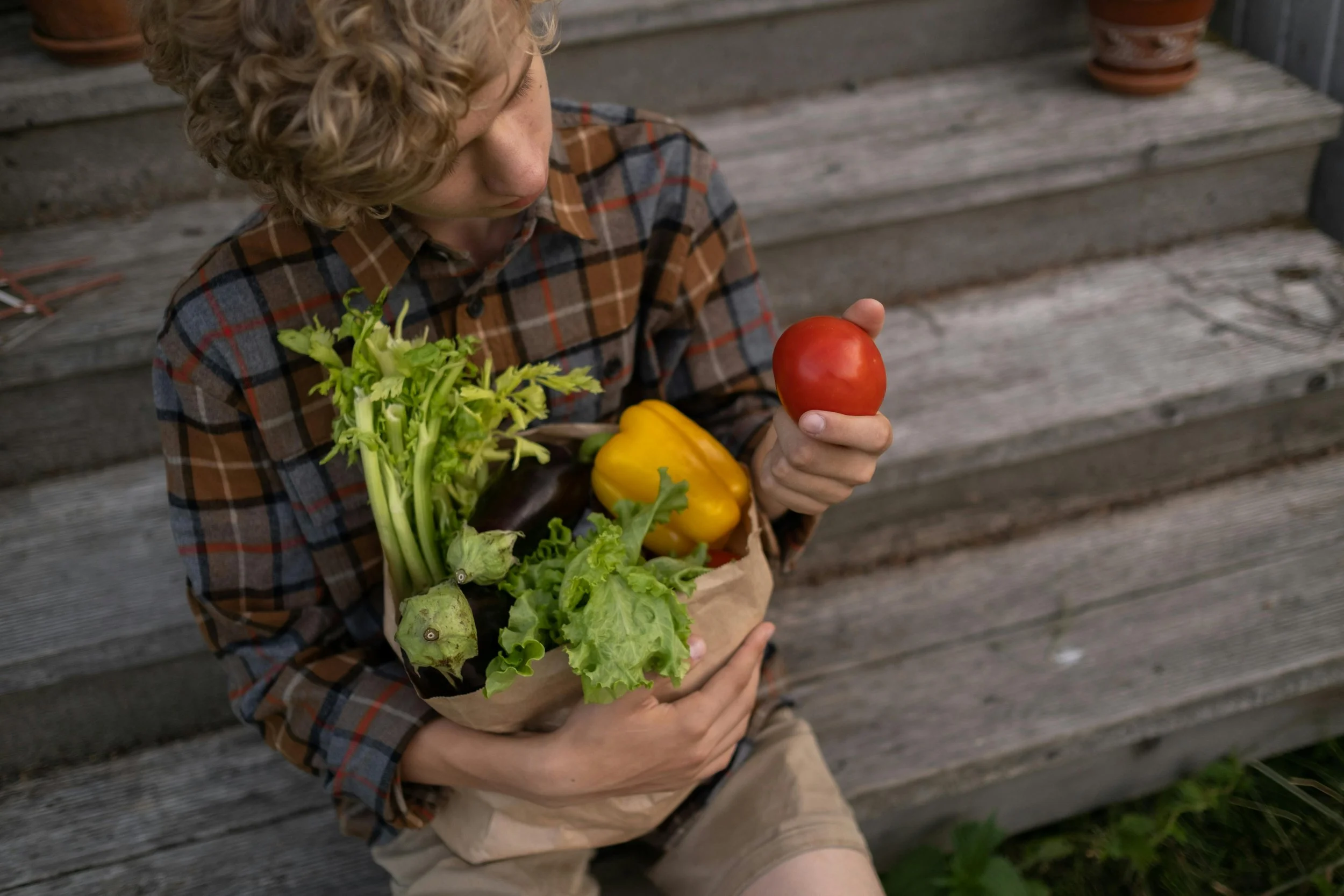 Young athlete holding a bag of fresh vegetables and a tomato, representing proper nutrition for youth athletes