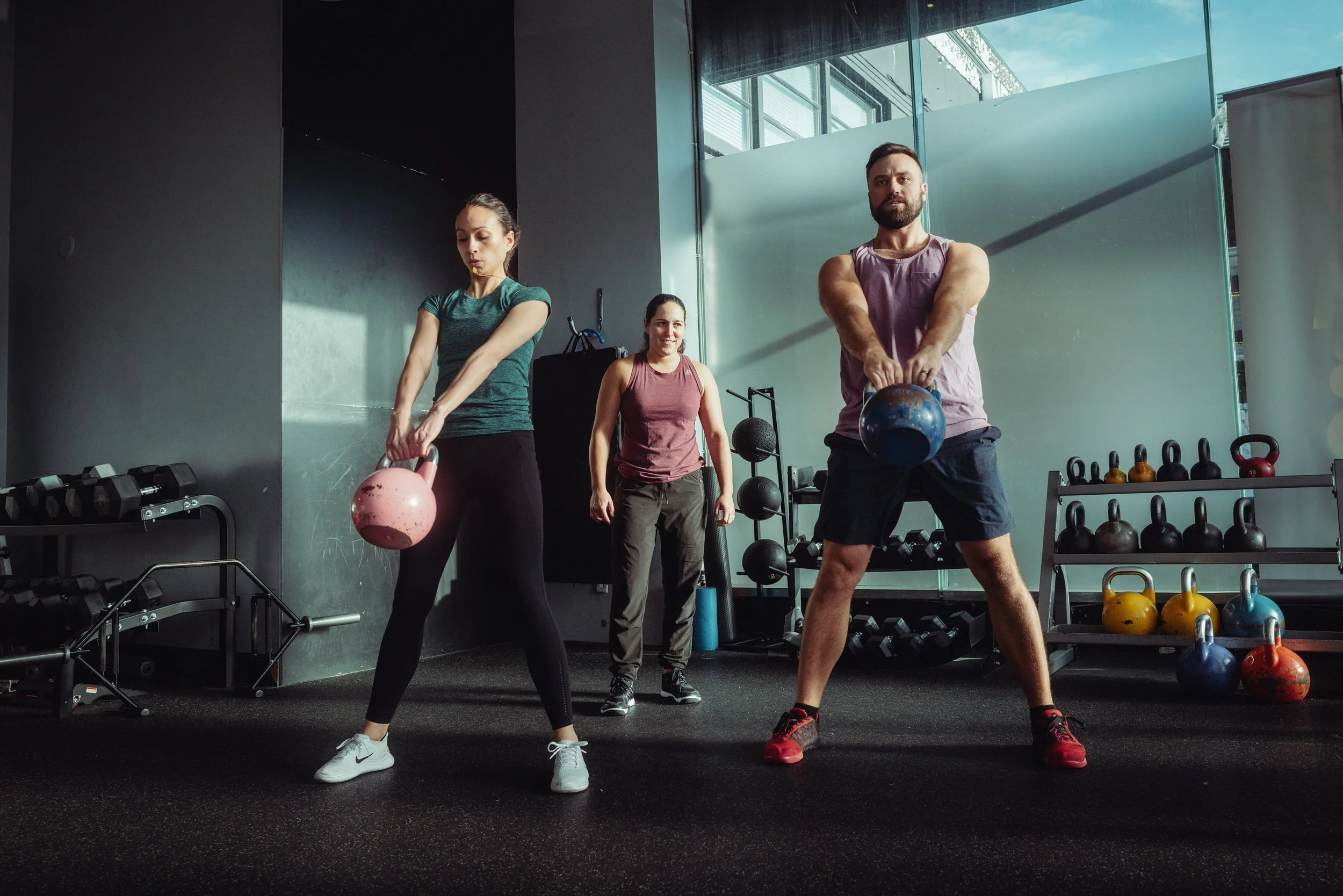Coach leading two clients through kettlebell swings during group training at Avos Strength