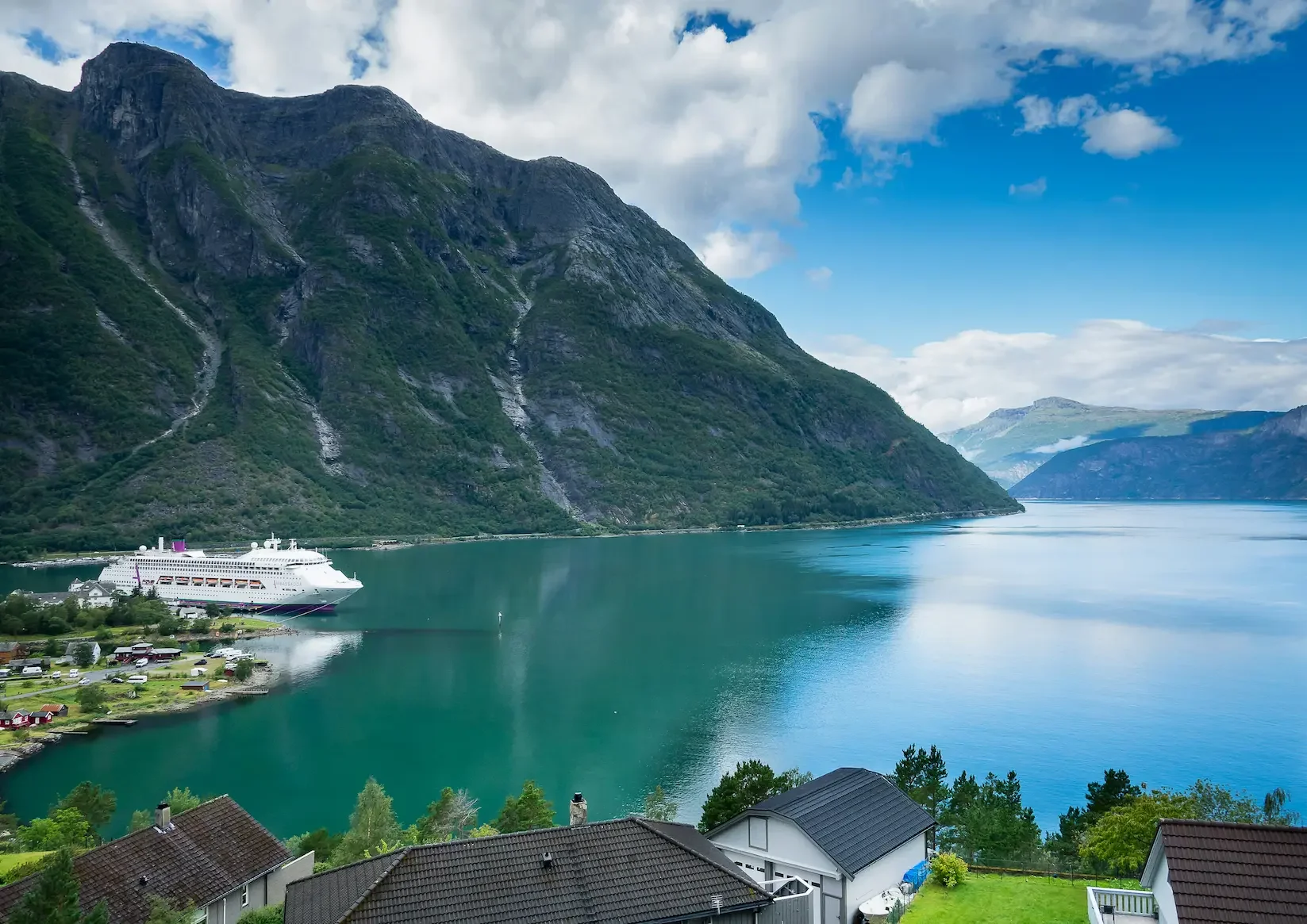 Cruise ship moored in the Norwegian Fjords with dramatic cliffs rising behind