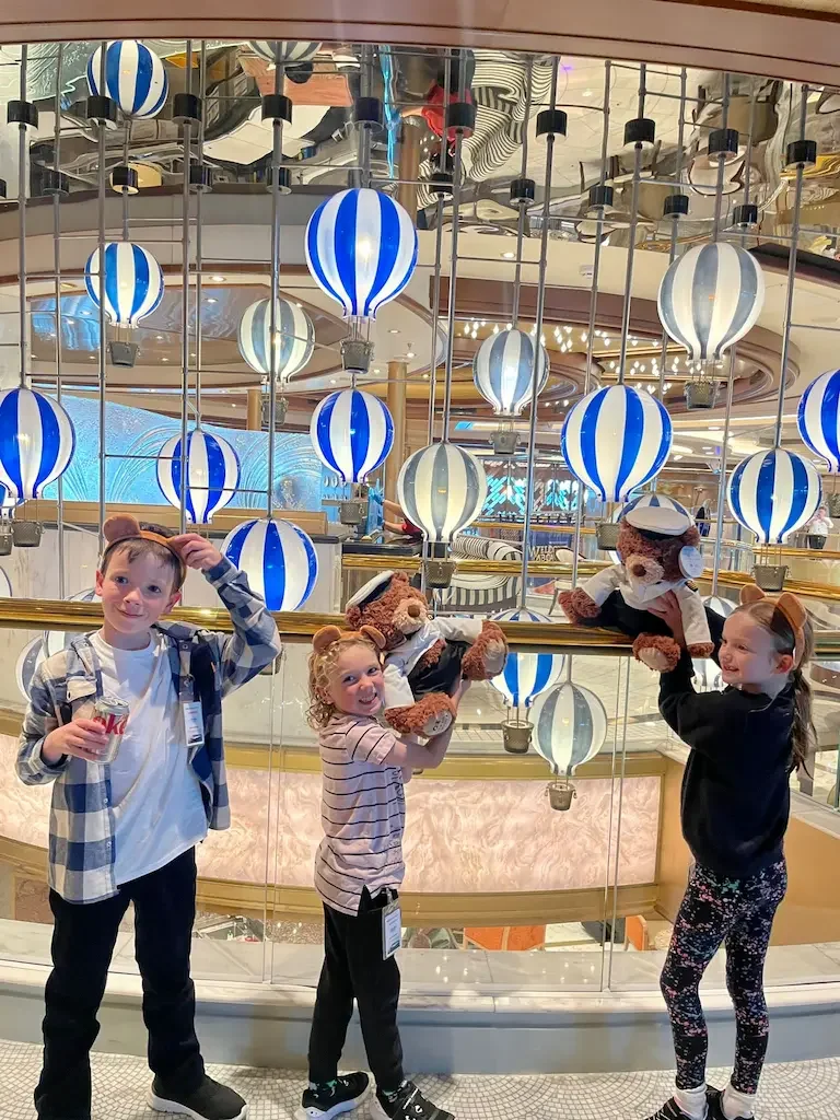 Children posing on Sky Princess with striped glass balloons over the atrium