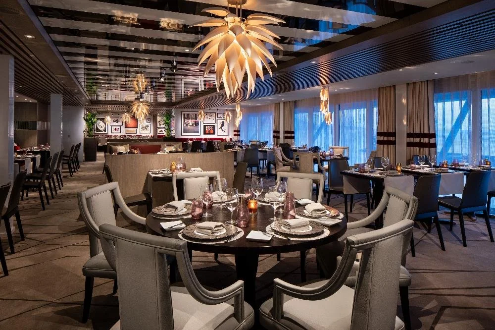 Interior of Luminae restaurant with tables set for dinner under designer chandeliers in The Retreat on Celebrity Cruises