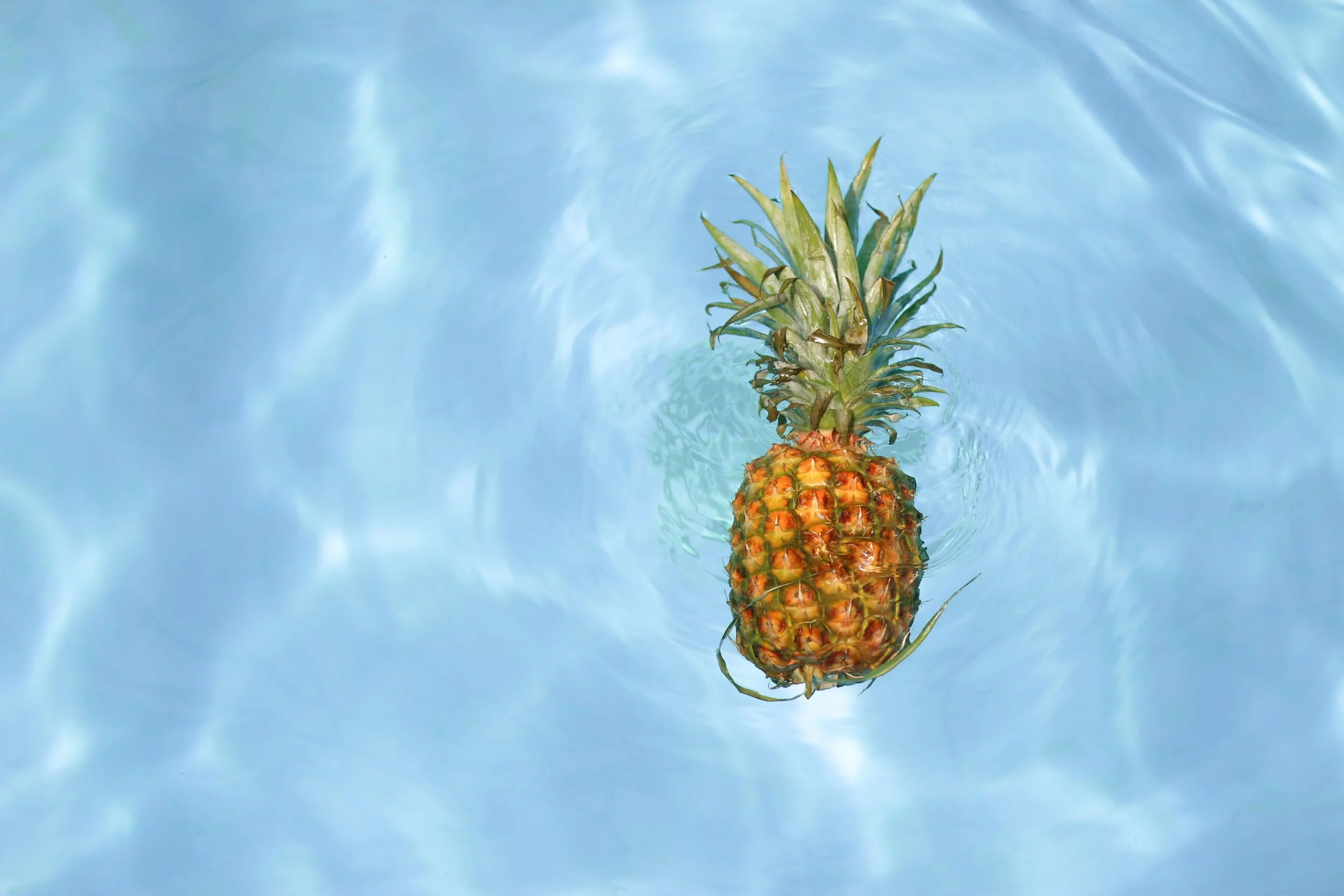 Pineapple floating in a swimming pool of blue water