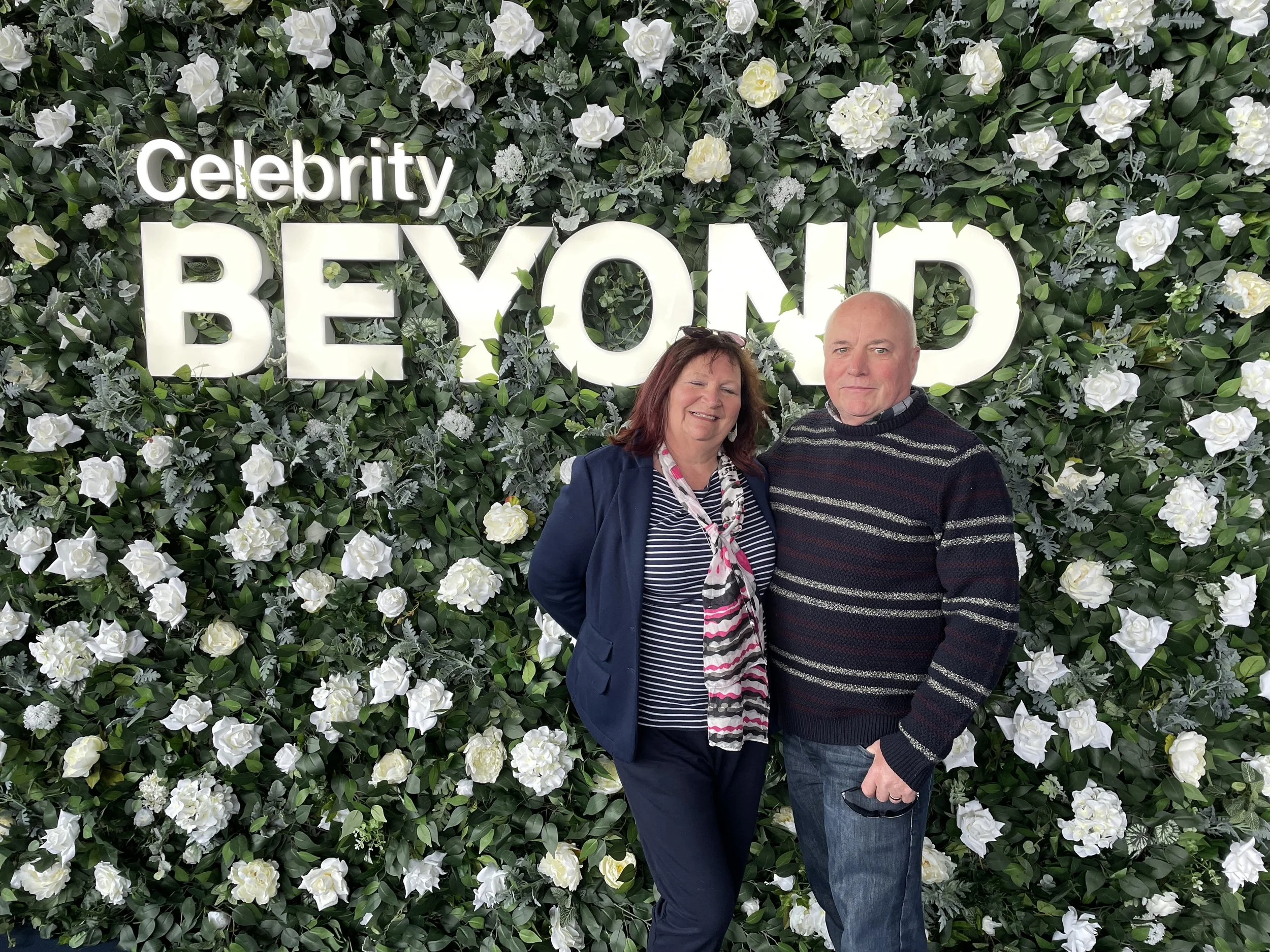 Kathy Taylor of Cruise Lowdown posing in front of Celebrity Beyond floral sign before boarding.