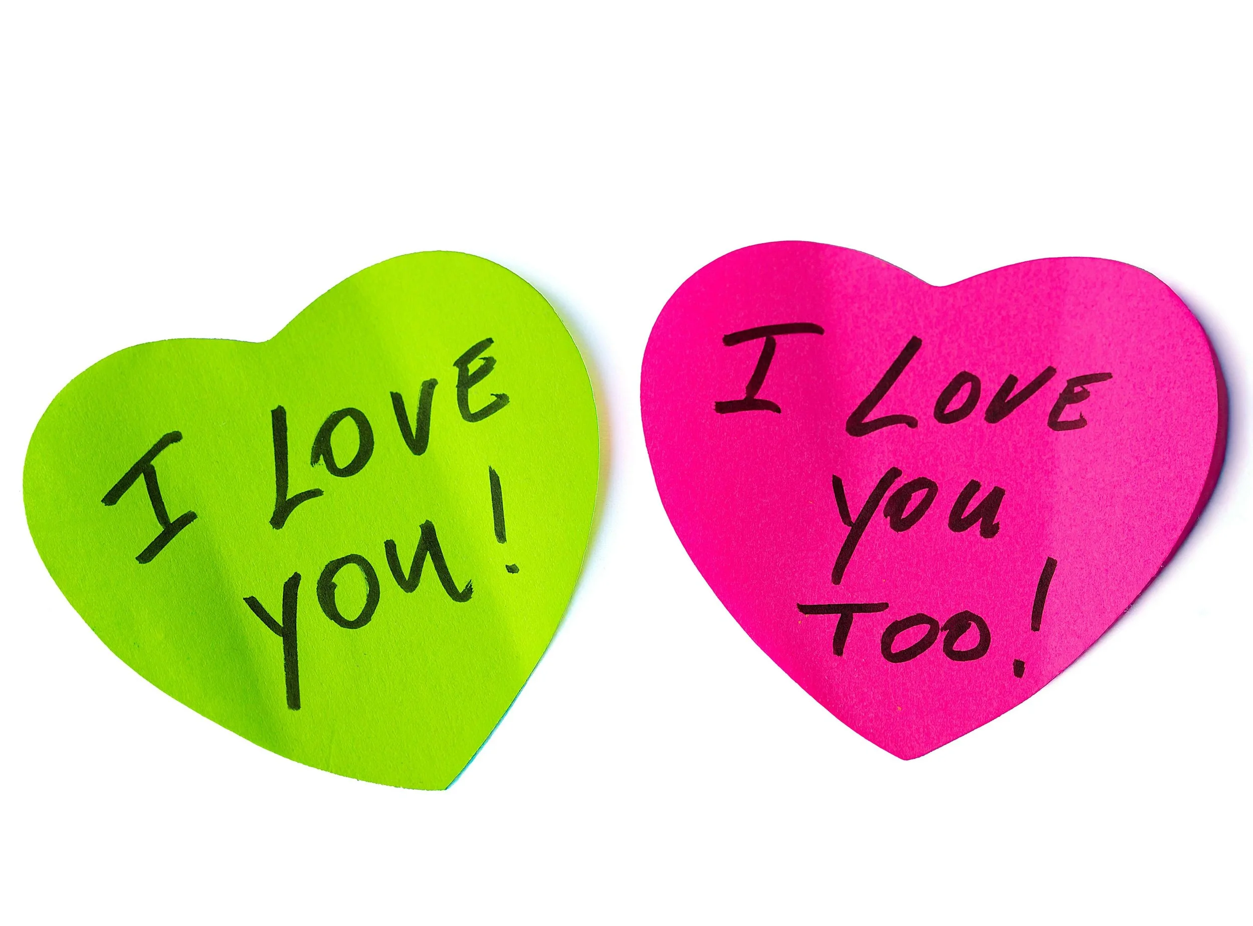 Green and a pink sticky note heart with love notes on them