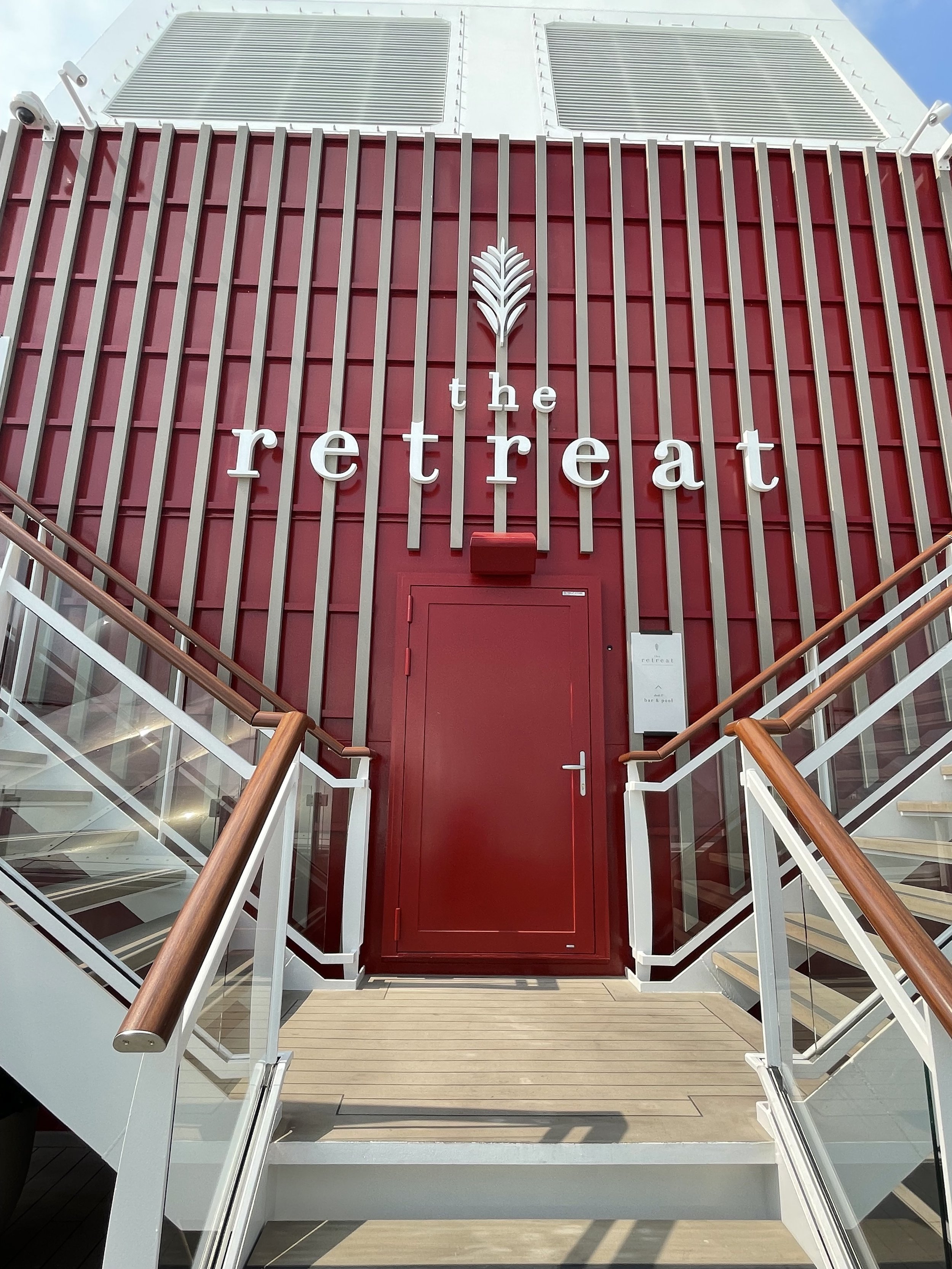 Dual staircases rise left and right of a central red door - the entrance to The Retreat on Celebrity Beyond.