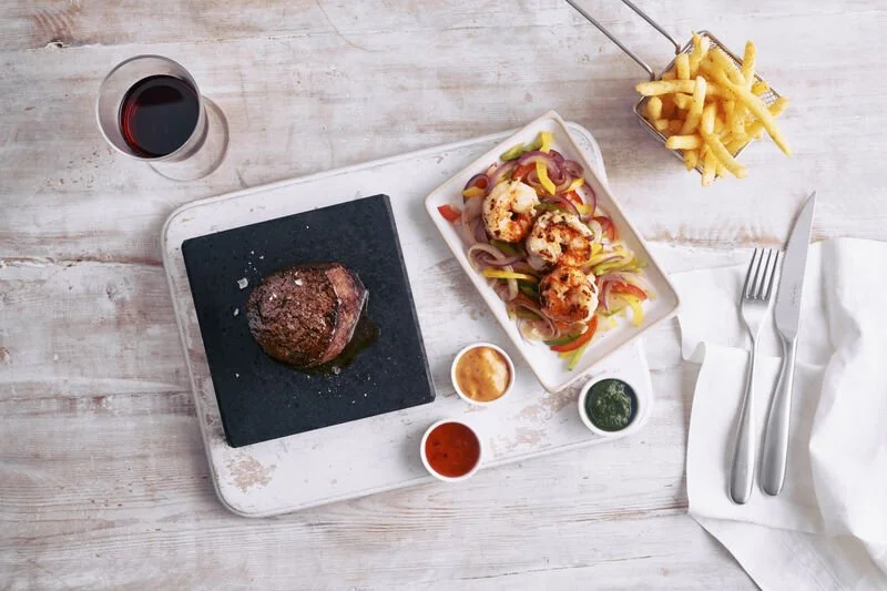 Flat lay of lava stone griddled filet steak, prawns (surf & turf) and fries from The Beach House restaurant on P& O Cruises