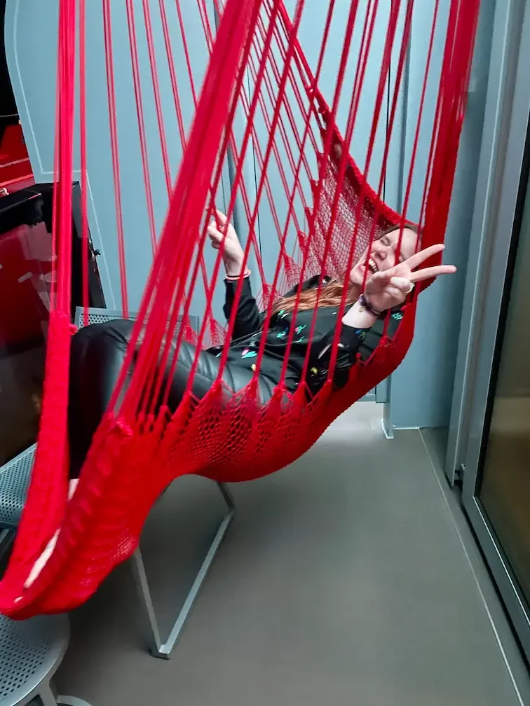 Female guest (sailor) enjoying Virgin Voyages signature red hammock on sea terrace cabin.