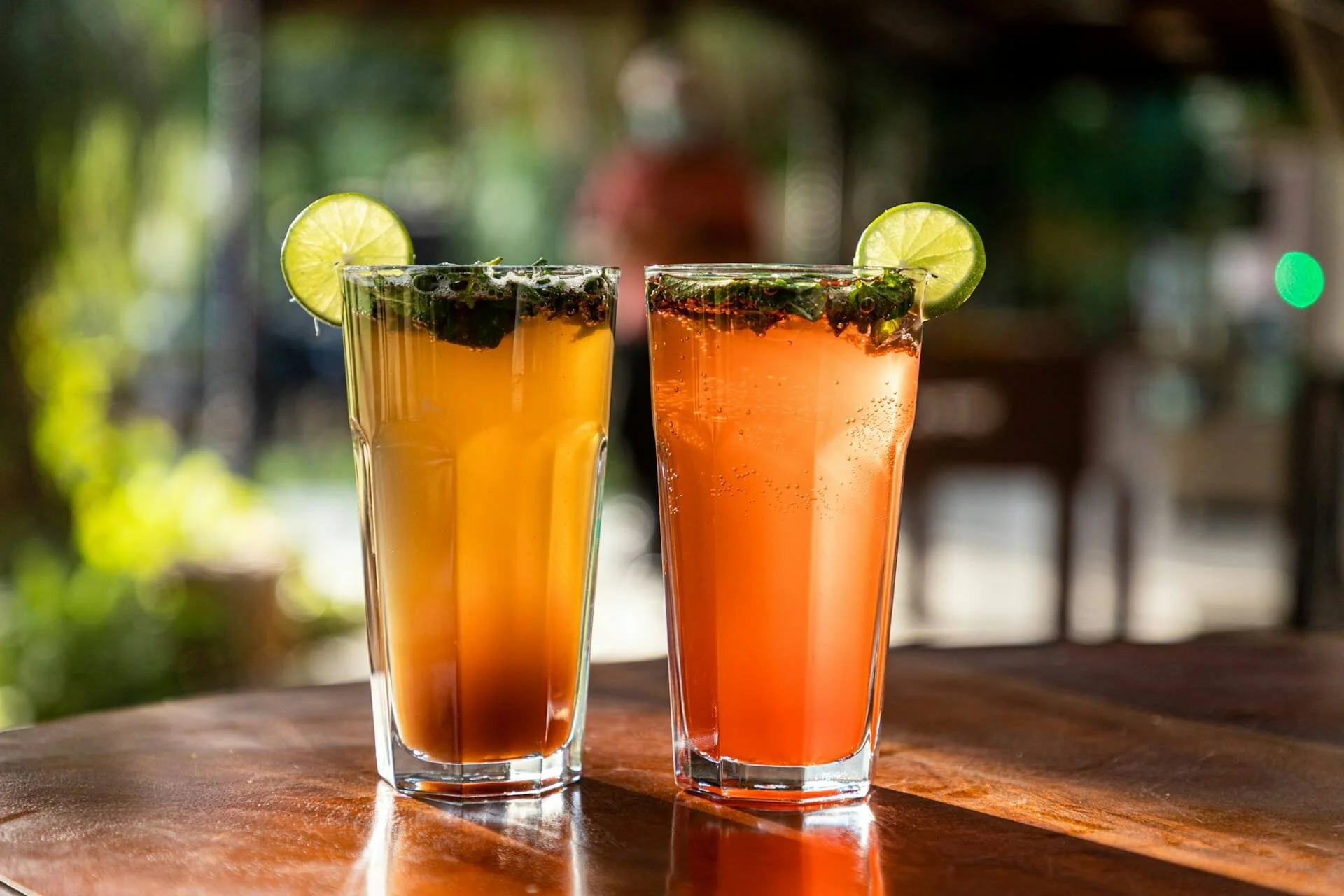 Two tall glasses of yellow and orang juices with mint and lime garnish