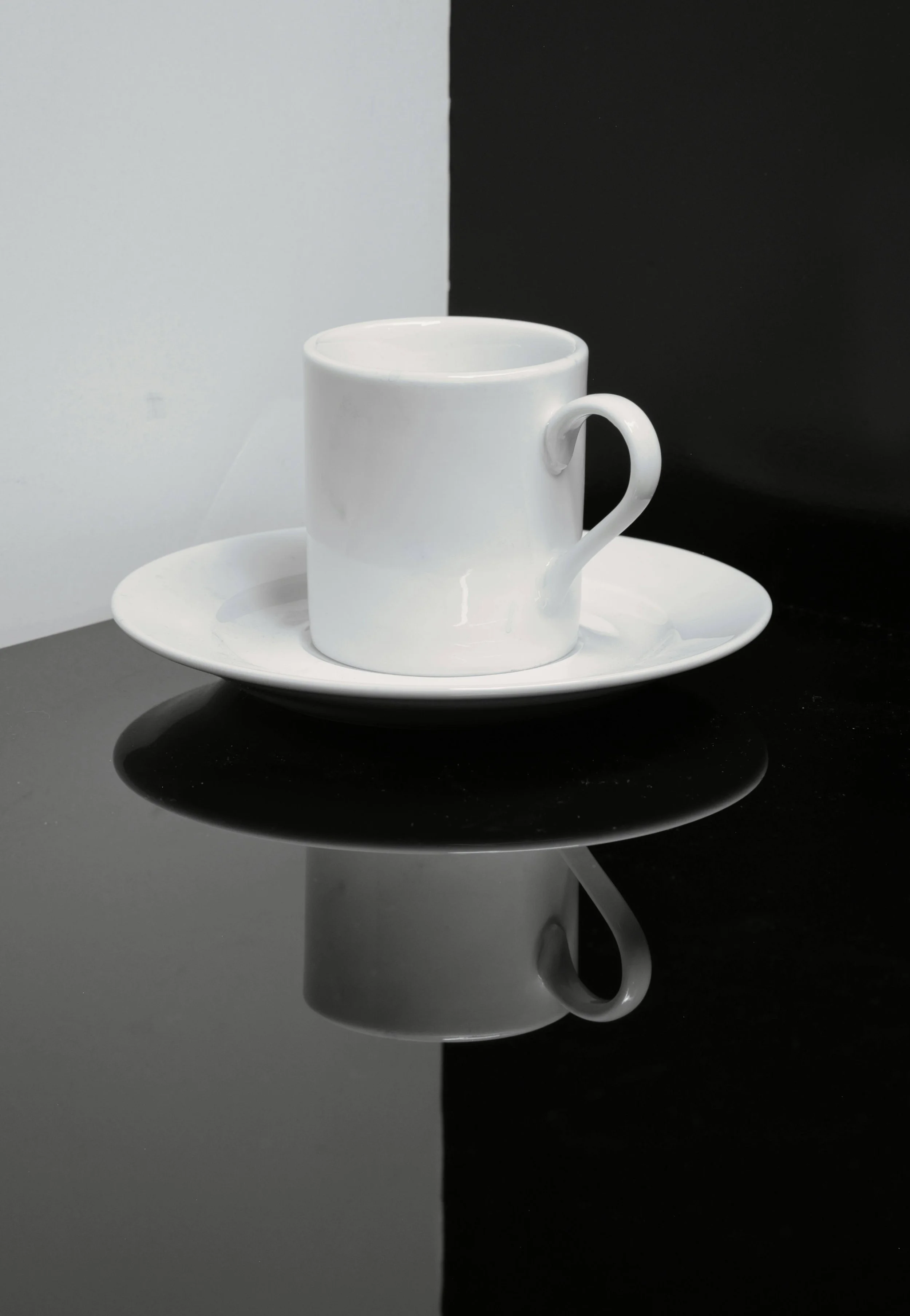A white cup and saucer on a black table top against a monochrome background